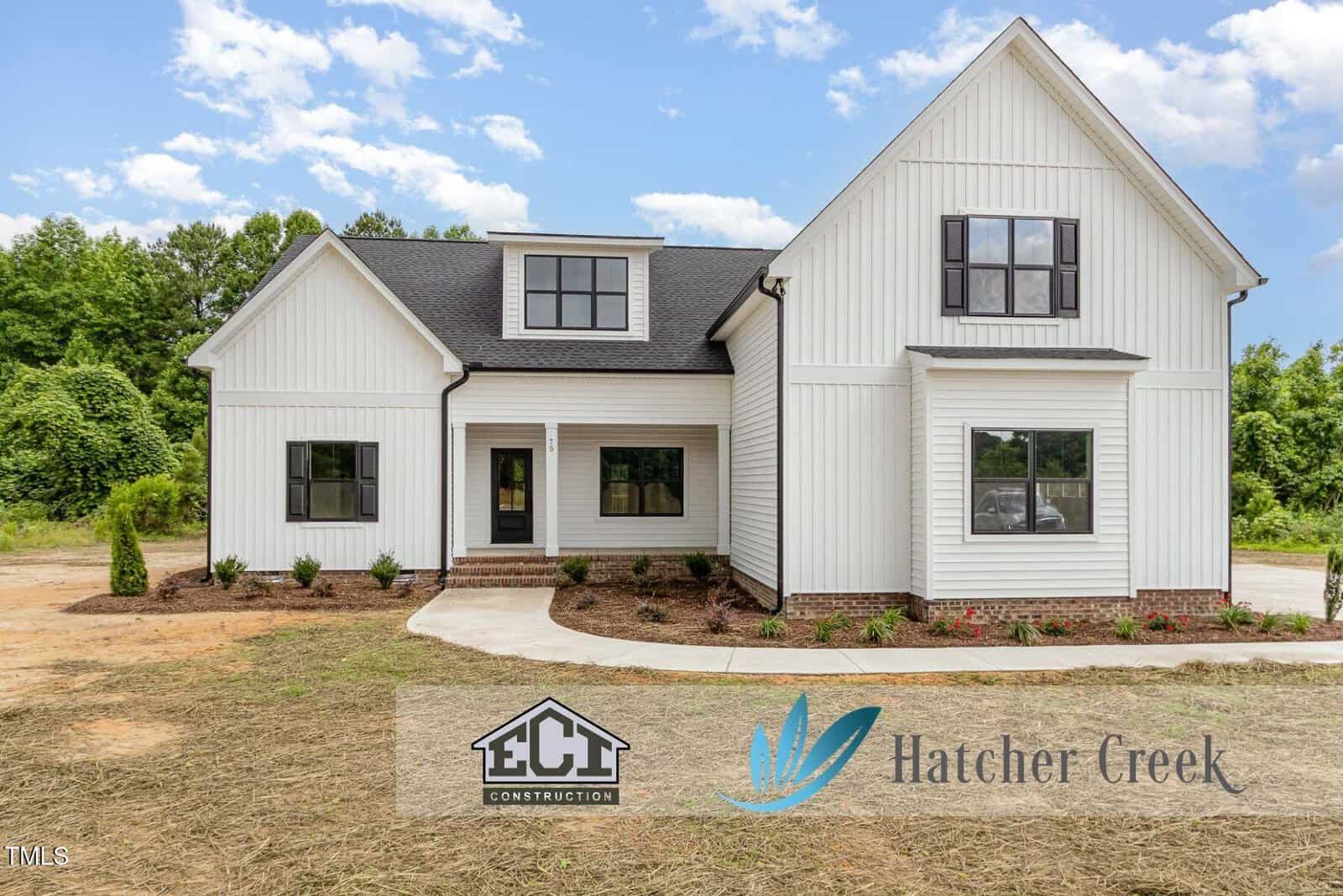 Modern white two-story house with black trim, a gable roof, front porch, landscaped yard, and two logos at the bottom: ECI Construction and Hatcher Creek. Set at 105 Woodland Creek Way in Oxford, the home is framed by trees and a blue sky in the background.