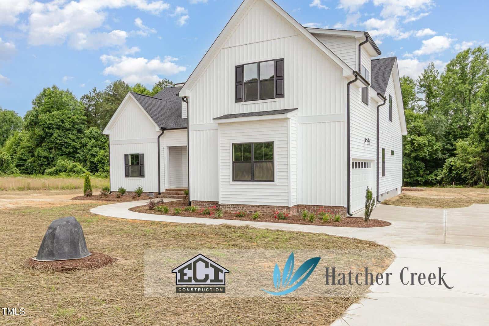 White modern farmhouse with black trim, a curved driveway, and minimal landscaping. Logos for "ECI Construction" and "Hatcher Creek" appear on the photo. Trees and blue sky are in the background.