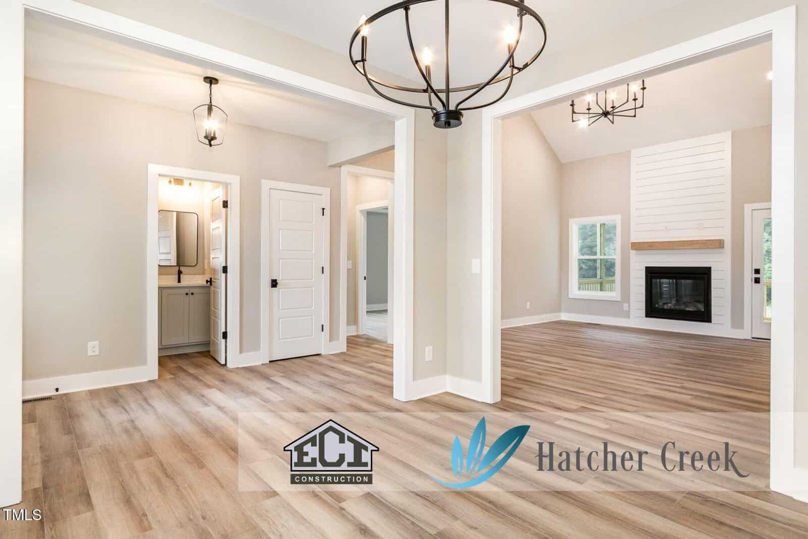 Bright modern home interior with light wood floors, white walls, black light fixtures, a visible bathroom, multiple doors, and a living area with a fireplace. Logos for ECI Construction and Hatcher Creek are at the bottom.