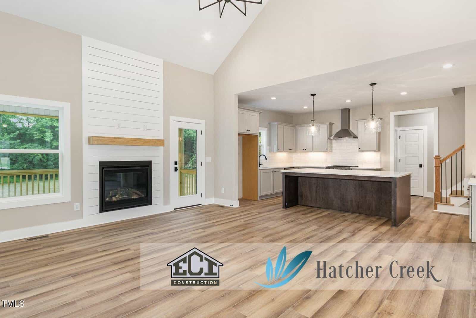 Modern open-concept living area with wood floors, a fireplace, large windows, and a kitchen with white cabinets and island. Logos for ECI Construction and Hatcher Creek are overlaid on the image.