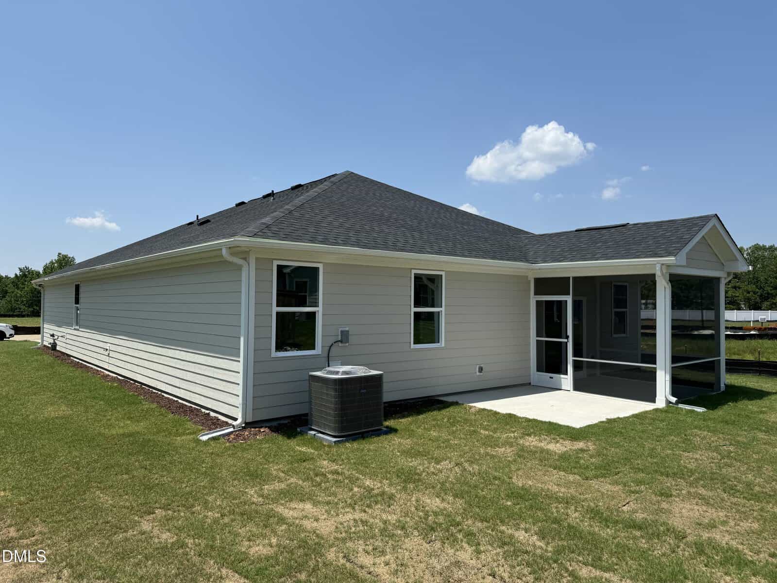 Single-story house with light siding, black roof, backyard AC unit, screened porch, and a grassy lawn under a blue sky with scattered clouds.