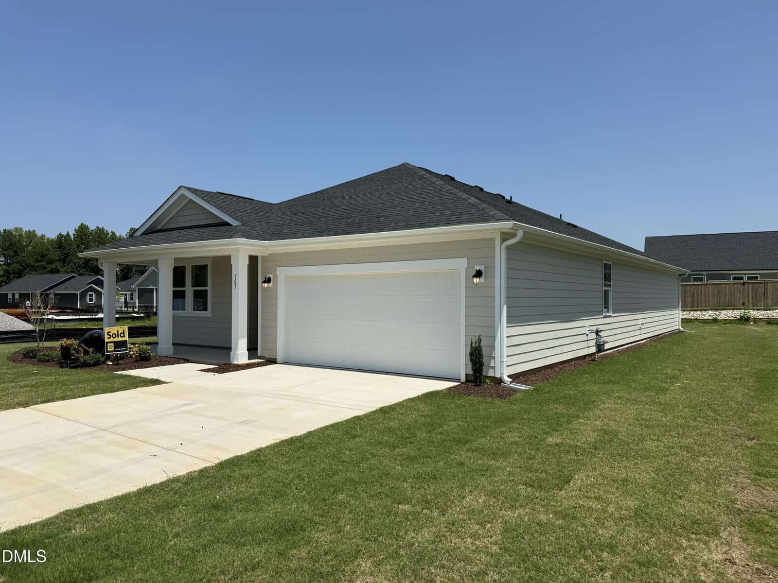 Single-story, white house with a black roof, two-car garage, and a "Sold" sign in the yard at 505 Purple Aster Street in Youngsville. The driveway and lawn are well-maintained, and the sky is clear and sunny.