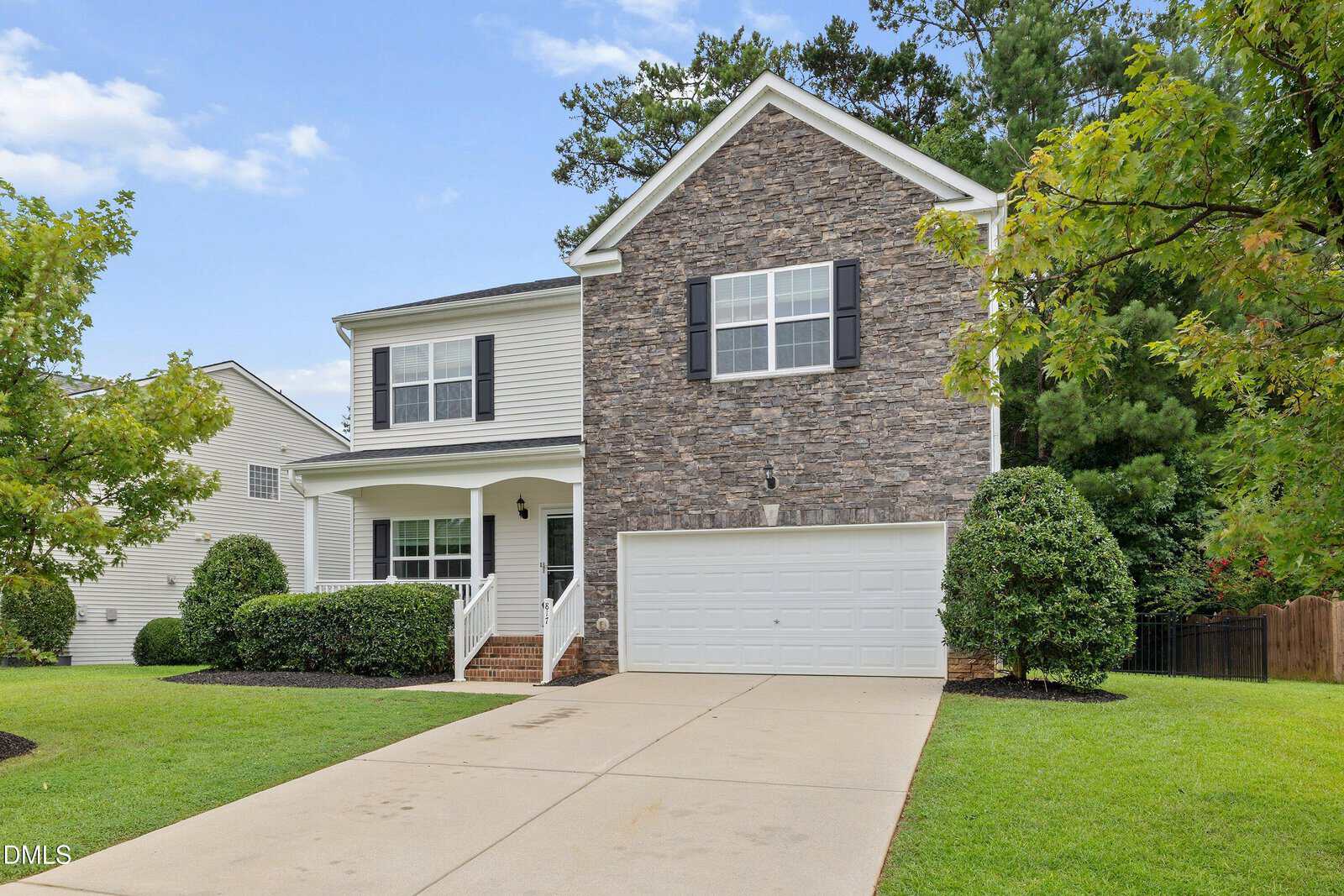 Two-story suburban house with a stone and siding exterior, black shutters, white trim, a front porch, two-car garage, and a well-kept lawn with shrubs and trees.