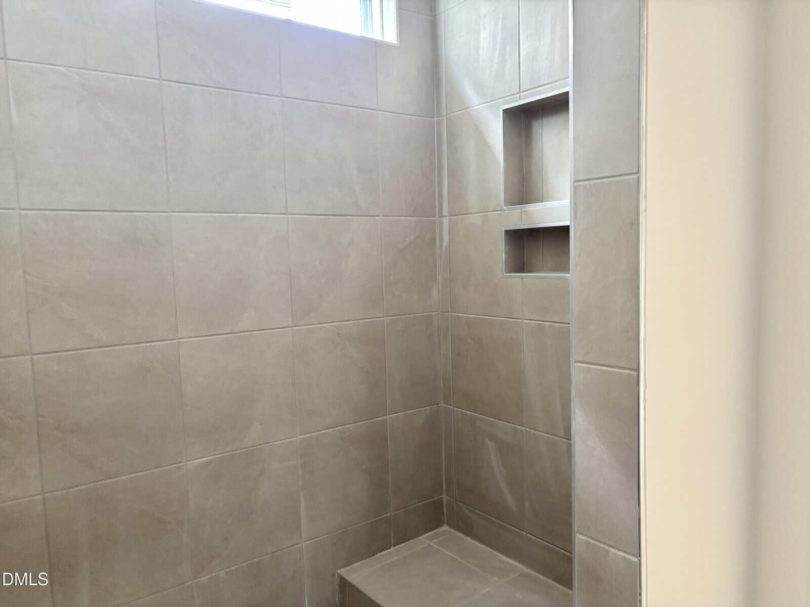 Tiled shower with a built-in bench, two wall niches for storage, and a small window providing natural light.