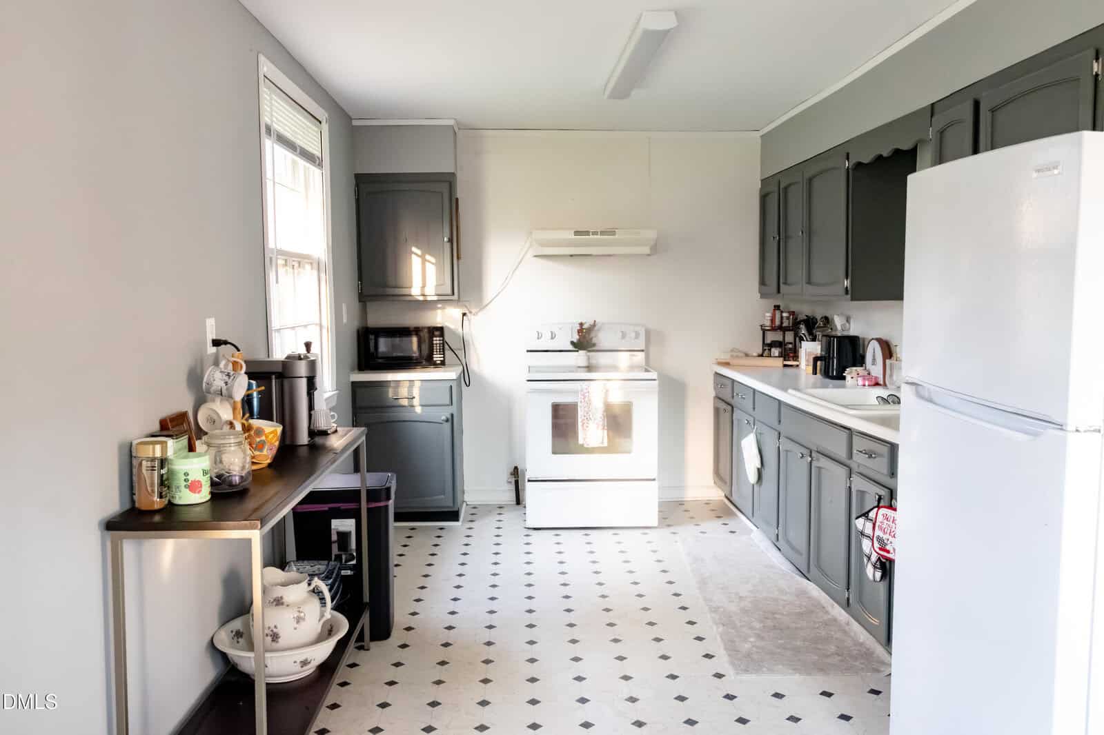 A kitchen with gray cabinets, white appliances, a coffee station on the left, and a stove with a range hood in the center. The floor has a white and black diamond pattern.