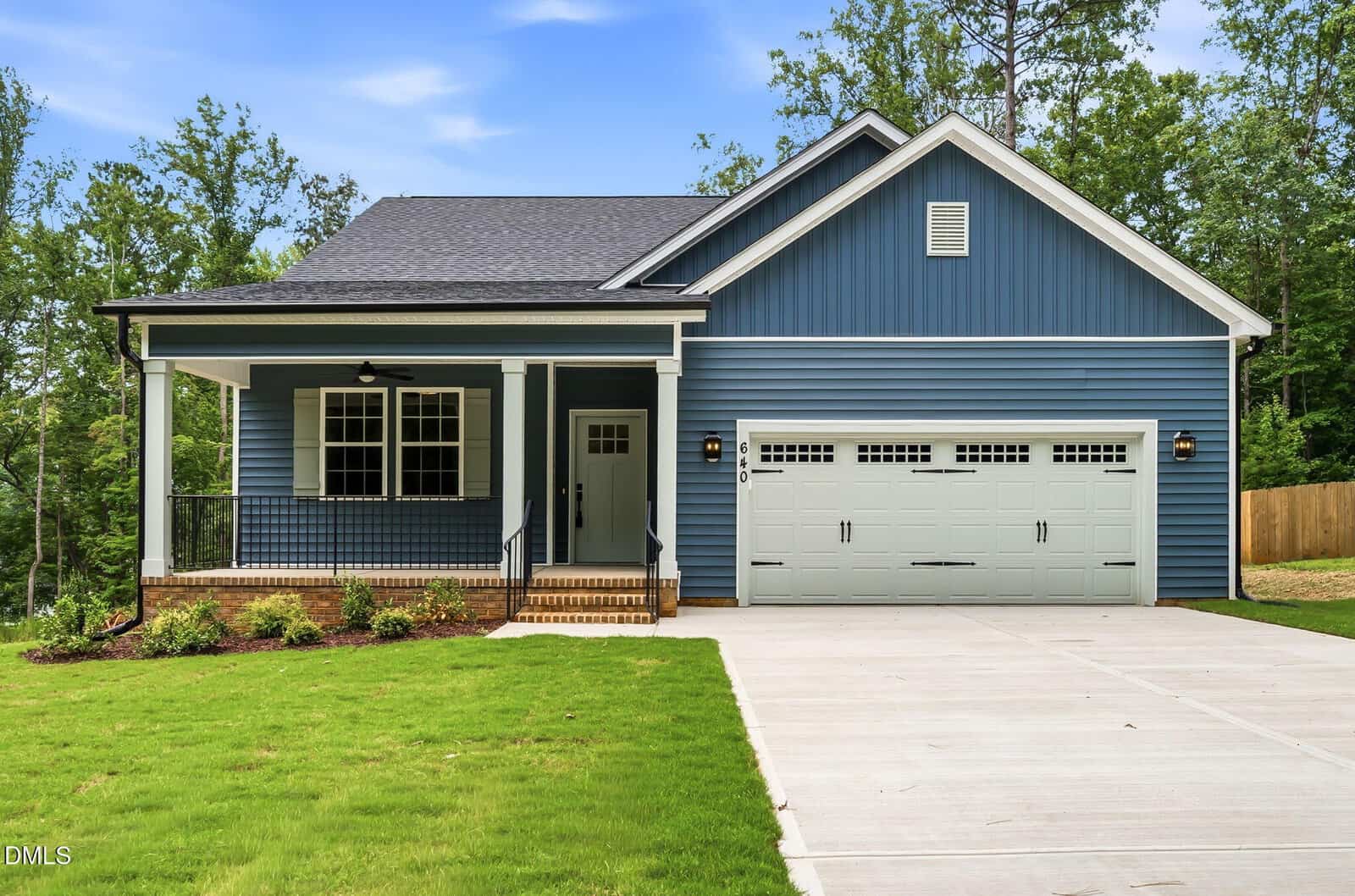 Nestled in the heart of Louisburg, this blue single-story house with white trim features a covered front porch and a double garage. Located at 640 Shawnee Drive, the home sits on a green lawn with a concrete driveway and is surrounded by trees and a wooden fence.