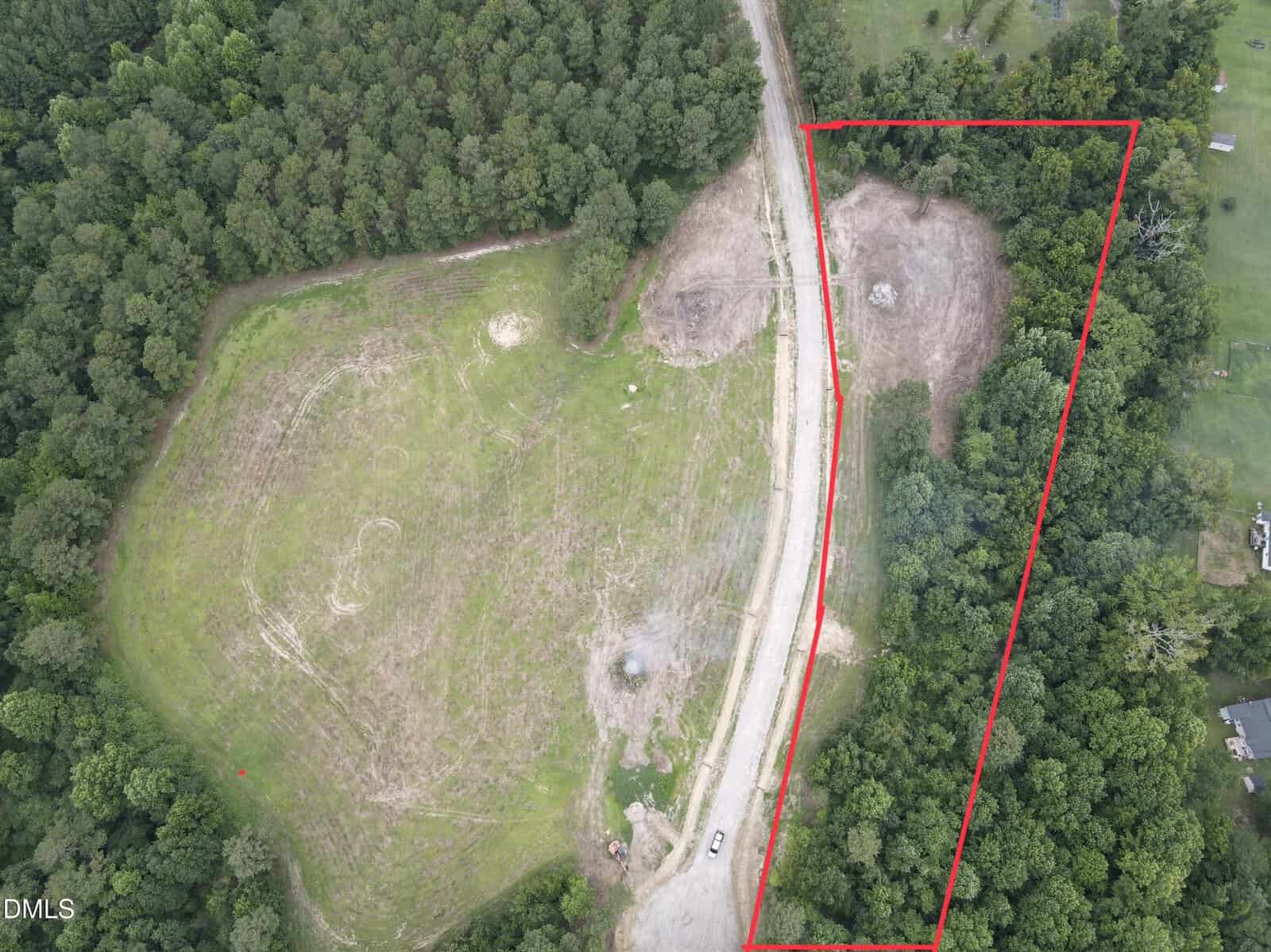 Aerial view of a cleared, grassy area bordered by dense trees at 1 Hidden Dreams Way, Zebulon. A dirt road curves through the scene. A section on the right, outlined in red, includes additional cleared land and forest. A small vehicle is parked near the road.
