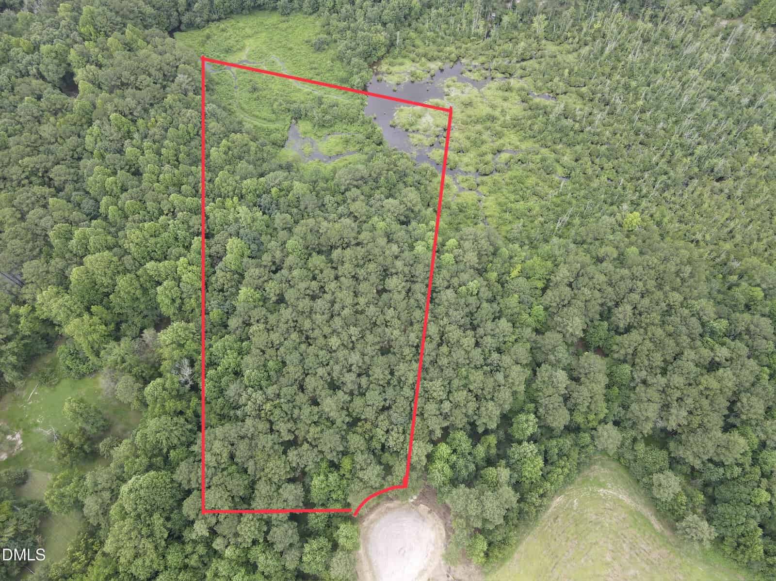 Aerial view of a wooded area with a dirt clearing at the bottom near 2 Hidden Dreams Way Road, Zebulon. The land is outlined in red, clearly showing boundaries. A small pond and marshy area are visible near the top, and dense forest surrounds the outlined plot.
