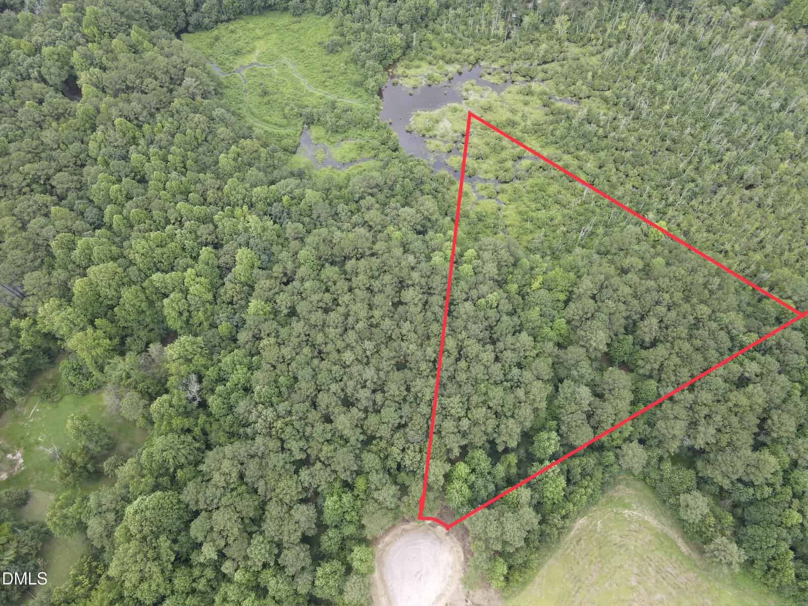 Aerial view of a forested area along 3 Hidden Dreams Way Road, Zebulon, with a triangular section outlined in red. There is a round cleared area at the bottom of the outlined section and a pond surrounded by trees near the top of the image.