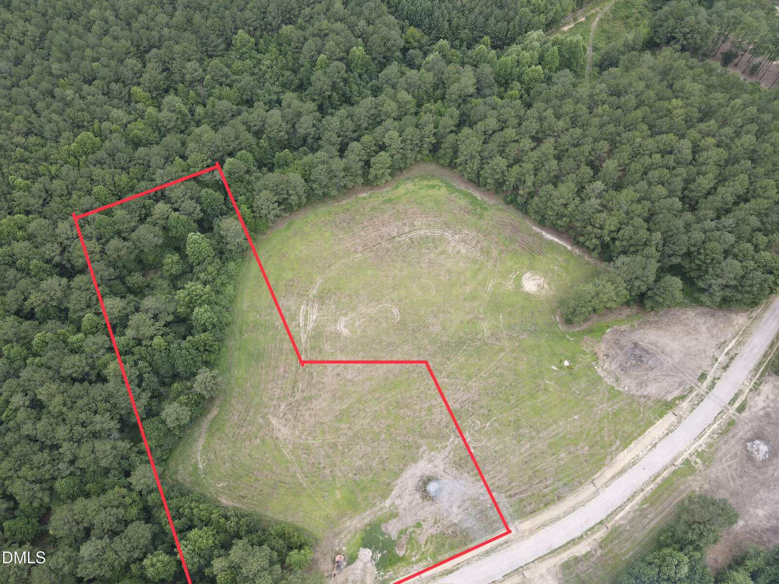 Aerial view of a partially cleared grassy field bordered by dense trees, with a section outlined in red near 4 Hidden Dreams Way Road in Zebulon. A dirt road runs alongside the field, and some cleared patches and debris are visible near the road.