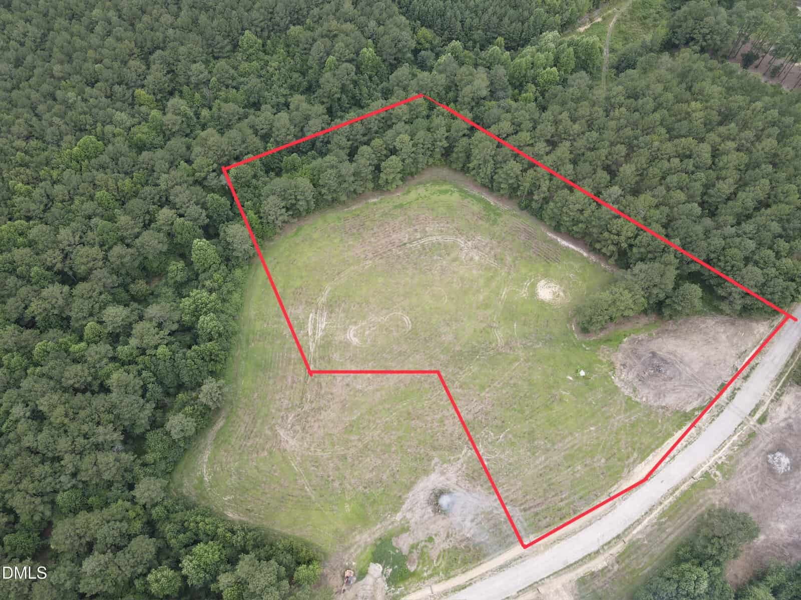 Aerial view of a forested area in Zebulon with a cleared grassy plot outlined in red. The plot, located off 5 Hidden Dreams Way Road, is bordered by trees on most sides and a dirt road along one edge. Some construction materials or debris are visible near the road.