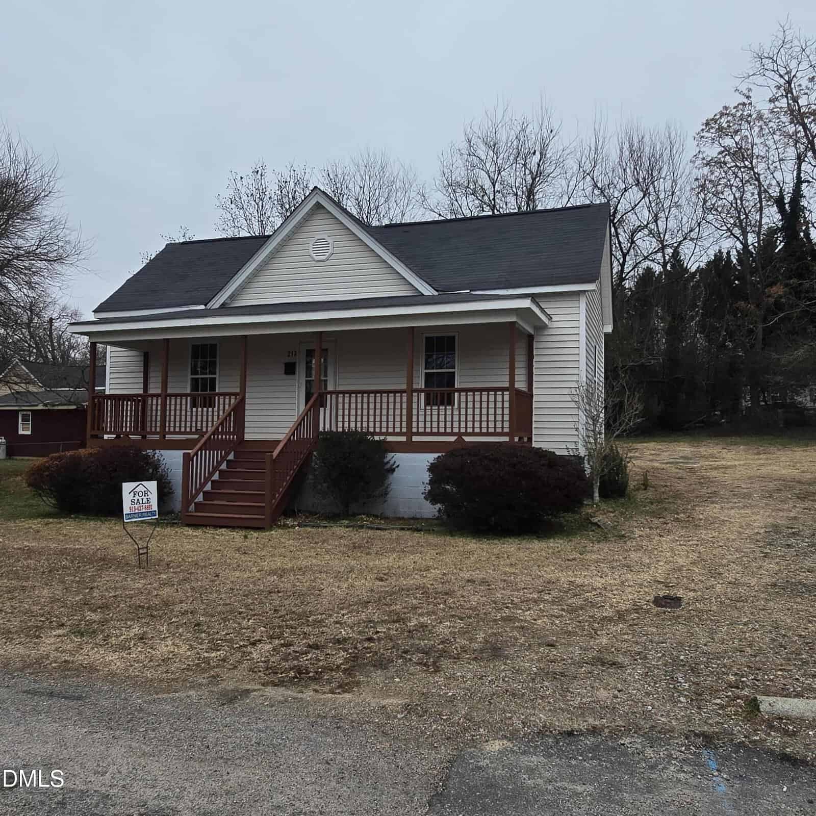 A single-story white house with a dark roof and red trim, featuring a front porch and steps, sits at 213 Cooke Street in Franklinton. There are shrubs in front, a for sale sign in the yard, and leafless trees in the background.