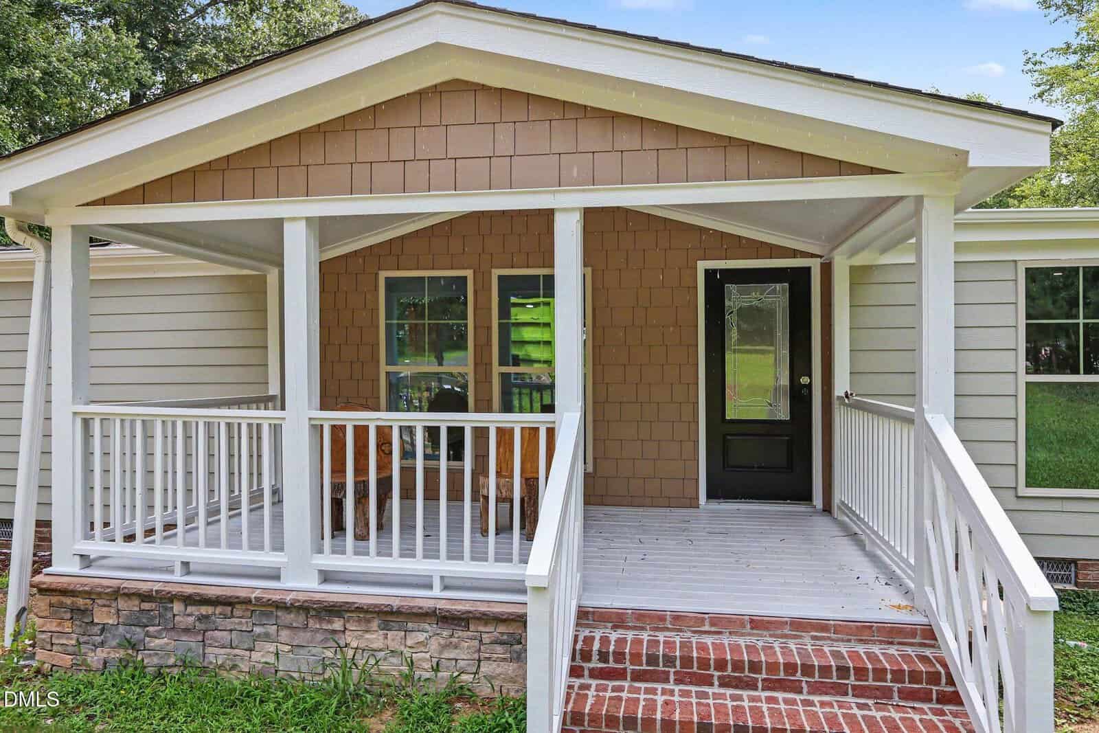 A single-story house in Creedmoor with a covered front porch, white railing, brick steps, and brown siding. Two windows and a black front door are visible at 1615 Hunters Trail, with grass and trees in the background.