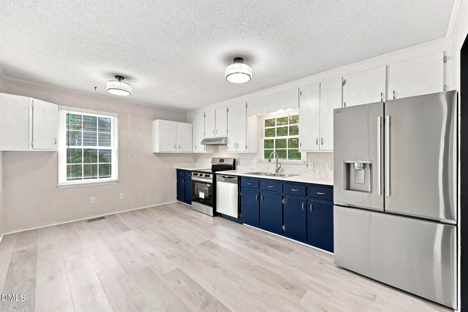 Modern kitchen with white upper cabinets, navy lower cabinets, stainless steel appliances, light wood flooring, two ceiling lights, and two windows with white blinds. The refrigerator has a water and ice dispenser.