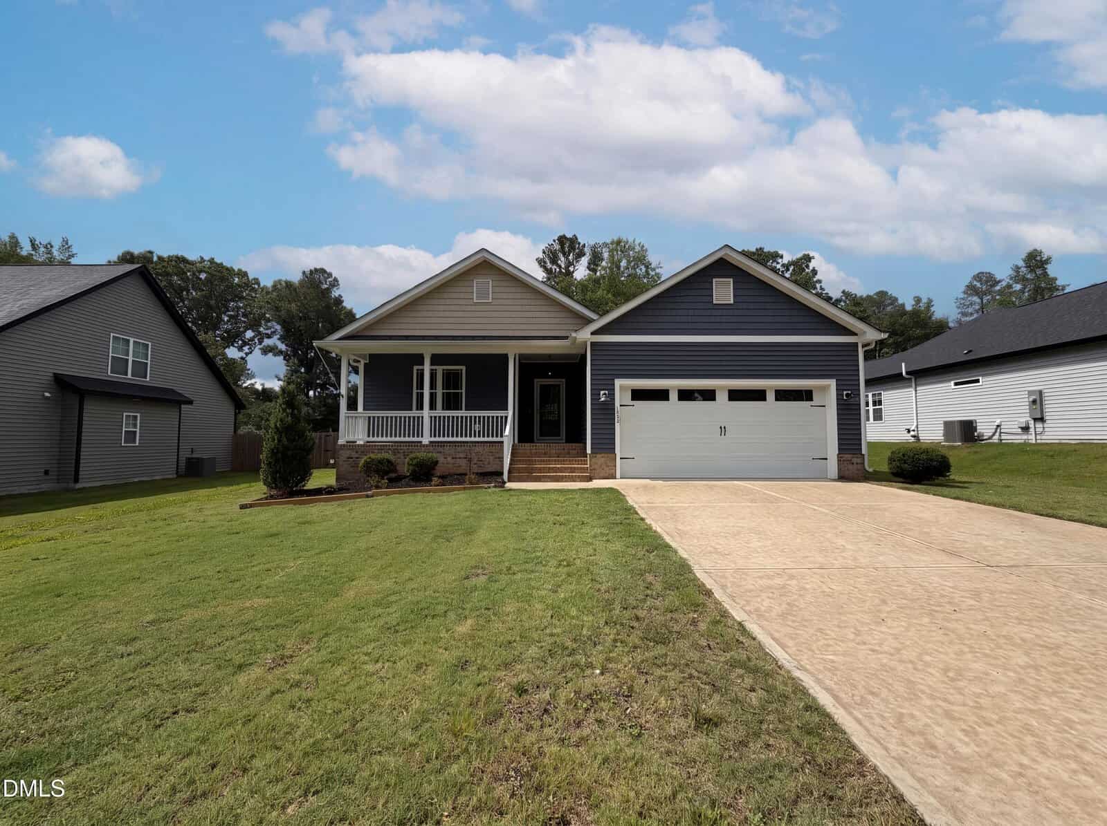 Located at 133 Ottawa Drive in Louisburg, this single-story blue house with white trim features a welcoming front porch and a spacious two-car garage. The home sits on a neatly mowed lawn with a concrete driveway, flanked by neighboring houses on either side under a partly cloudy sky.