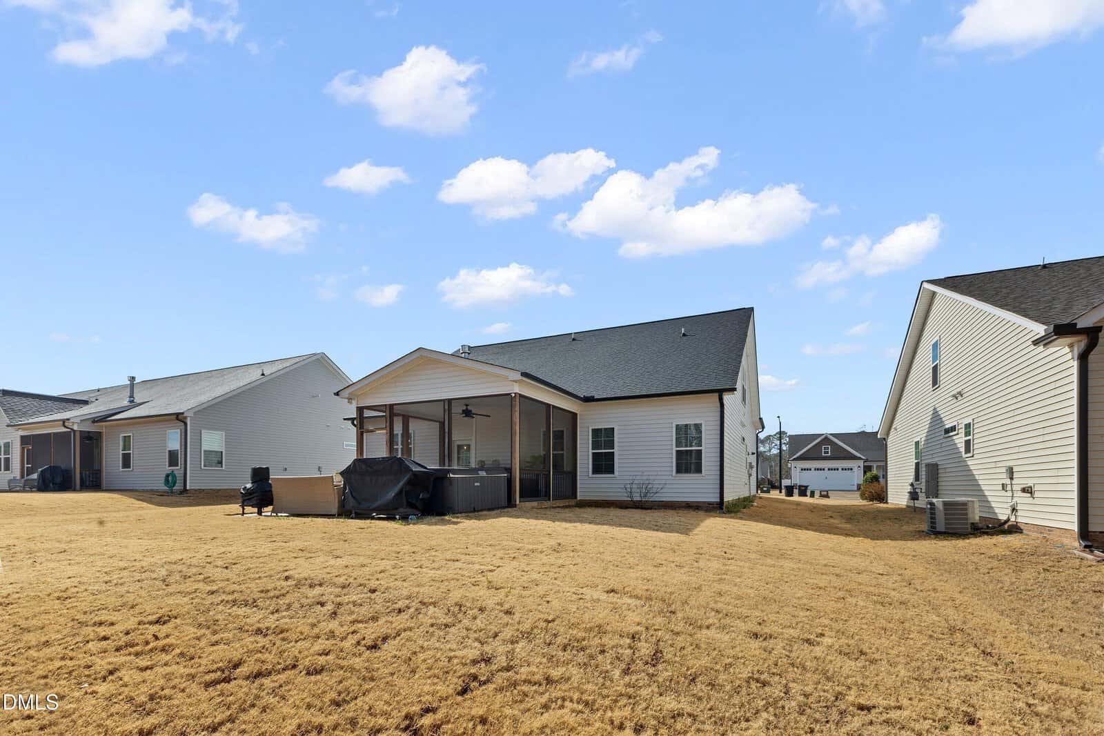 Three single-story houses with light-colored siding, covered patios, and fenced backyards are shown on a dry, yellowed grassy lawn under a partly cloudy blue sky.