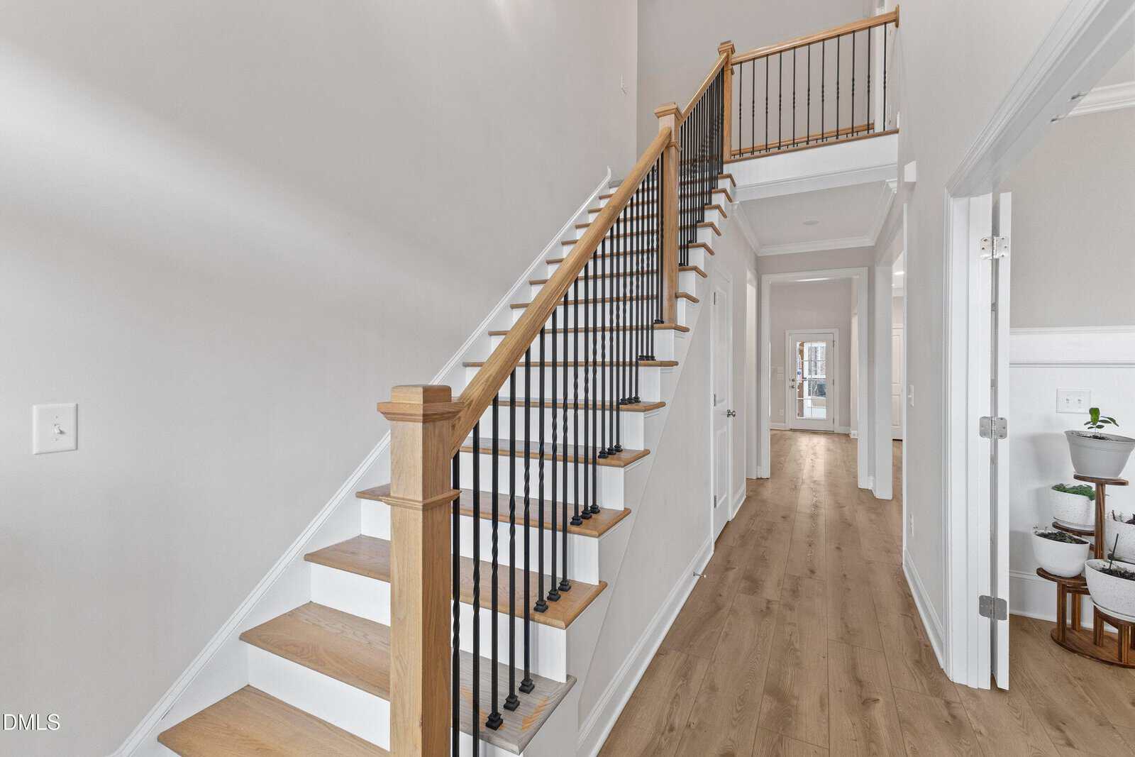 A modern hallway with light wood flooring, white walls, a staircase with wooden handrail and black balusters, and several open doors leading to other rooms.