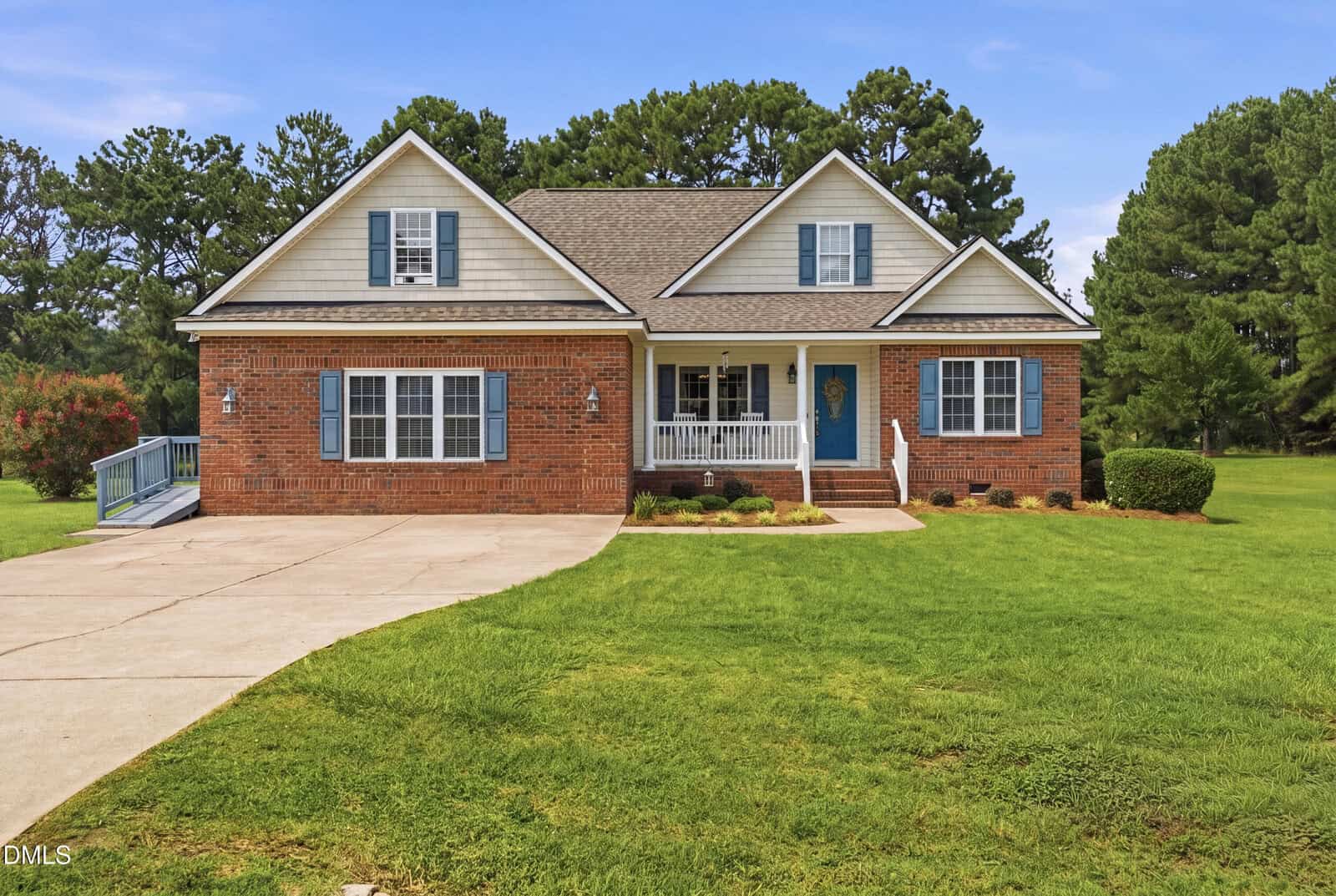Charming single-story brick house at 40 Perry Lane, Zebulon, featuring white trim, blue shutters, and a blue front door. The home offers a covered front porch, gabled roof, concrete driveway, and is surrounded by a large, neatly mowed lawn with trees in the background.