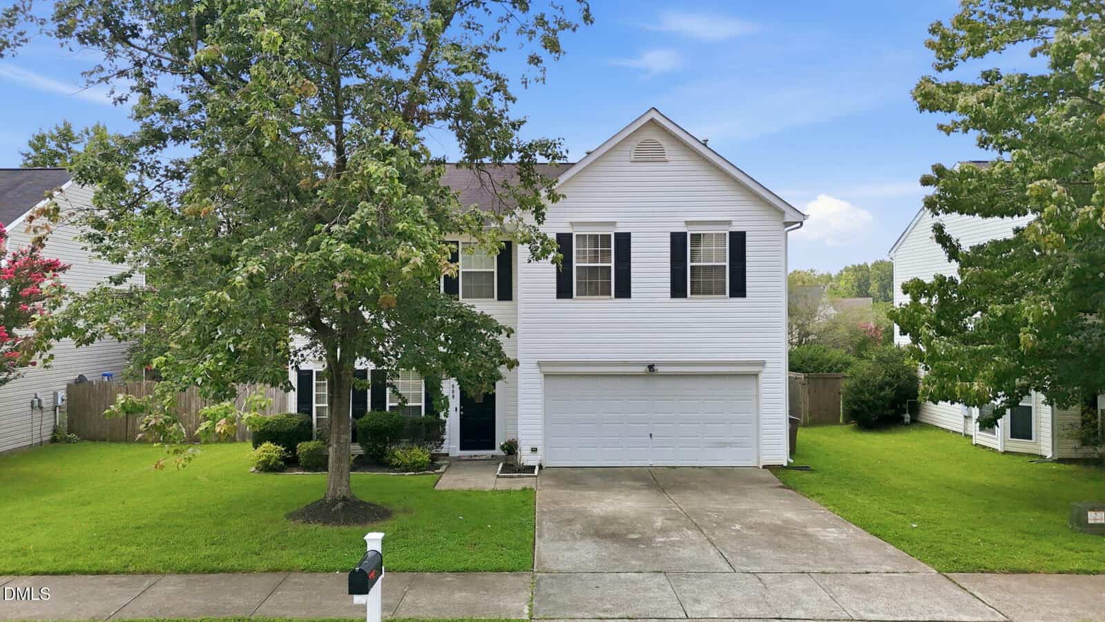 Two-story white house with black shutters, a double garage, and a concrete driveway located at 809 Stackhurst Way in Wake Forest. There are green lawns, a large tree in front, and a mailbox on the sidewalk. Neighboring houses are visible on both sides.
