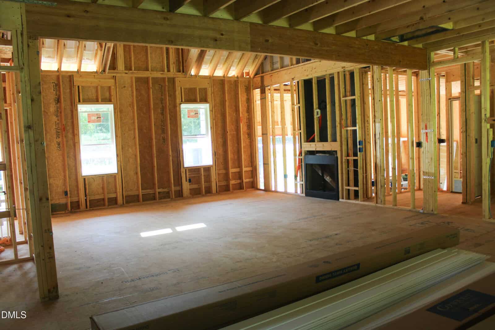 Framed room in a house under construction, with exposed wooden beams, unfinished walls, windows, and building materials stacked on the floor.