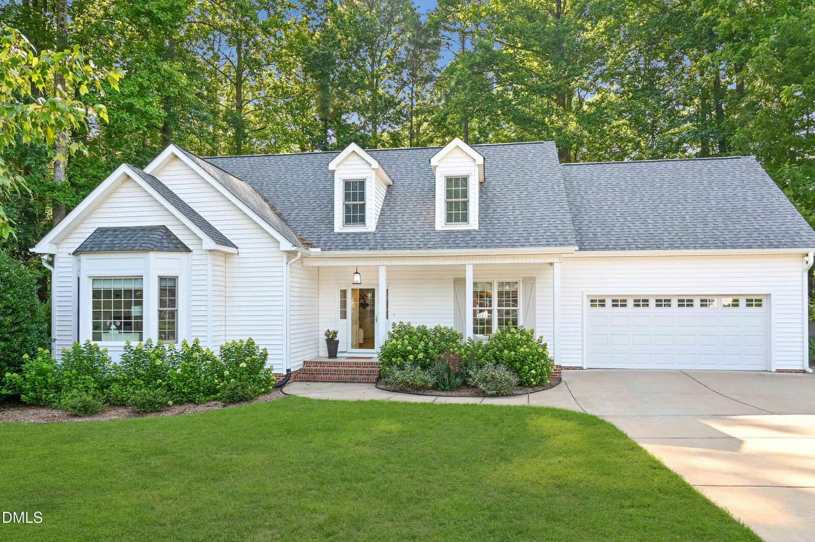 Charming single-story white house with gray roof, two dormer windows, and an attached two-car garage located at 25 Allyson Court in Youngsville. Enjoy a manicured lawn, small front porch with brick steps, and landscaped bushes. Surrounded by trees and set in a quiet residential neighborhood.
