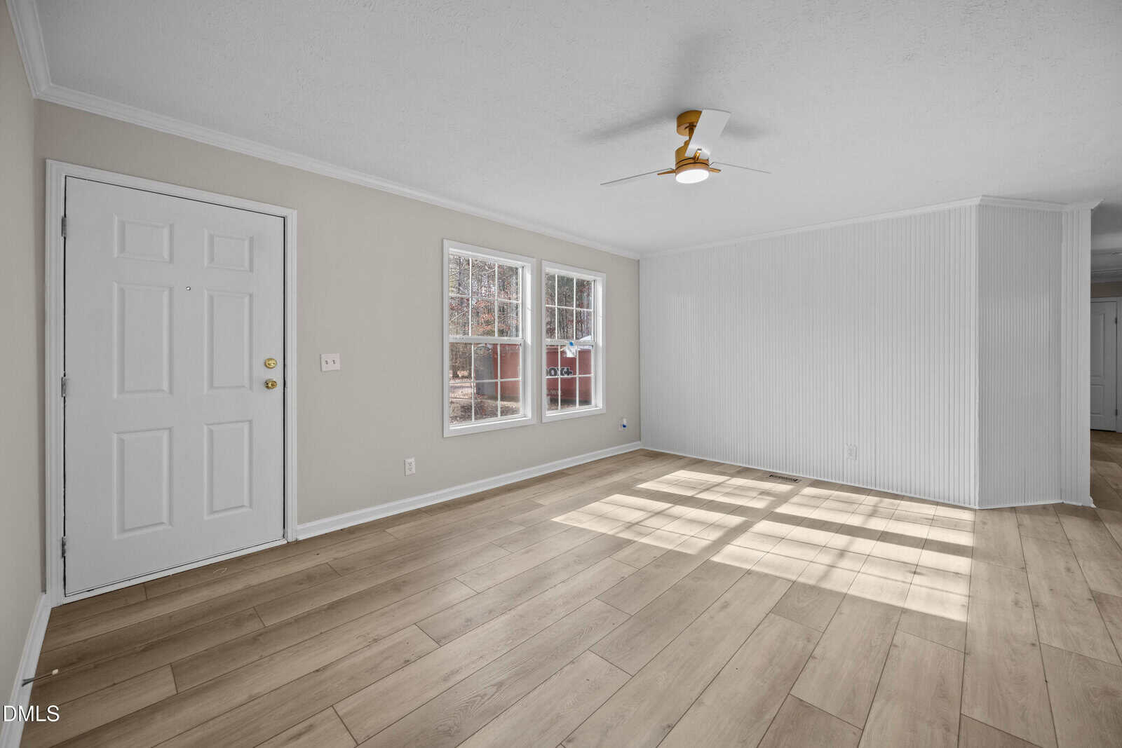 Bright, empty room with light wood floors, white walls, two windows, a white entry door, a ceiling fan, and sunlight streaming across the floor.