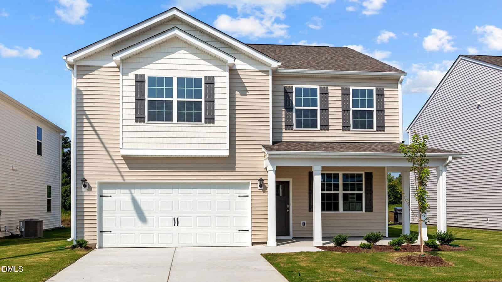 Charming two-story beige house located at 15 Winding River Way, Youngsville, featuring a welcoming front porch, white trim, and classic black shutters. There is a double garage, a small tree in the front yard, and the driveway leads directly to the street. The sky is mostly clear with just a few clouds drifting by.
