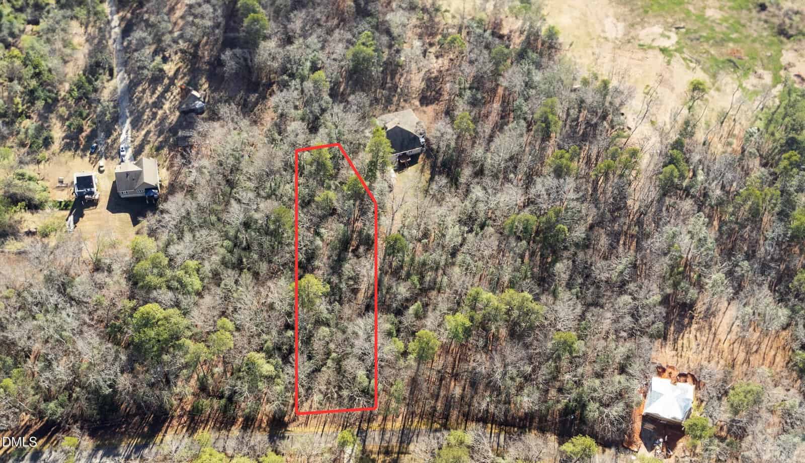 Aerial view of a wooded area with a rectangular plot of land outlined in red. There are several houses scattered around the plot, surrounded by dense trees and clearings.