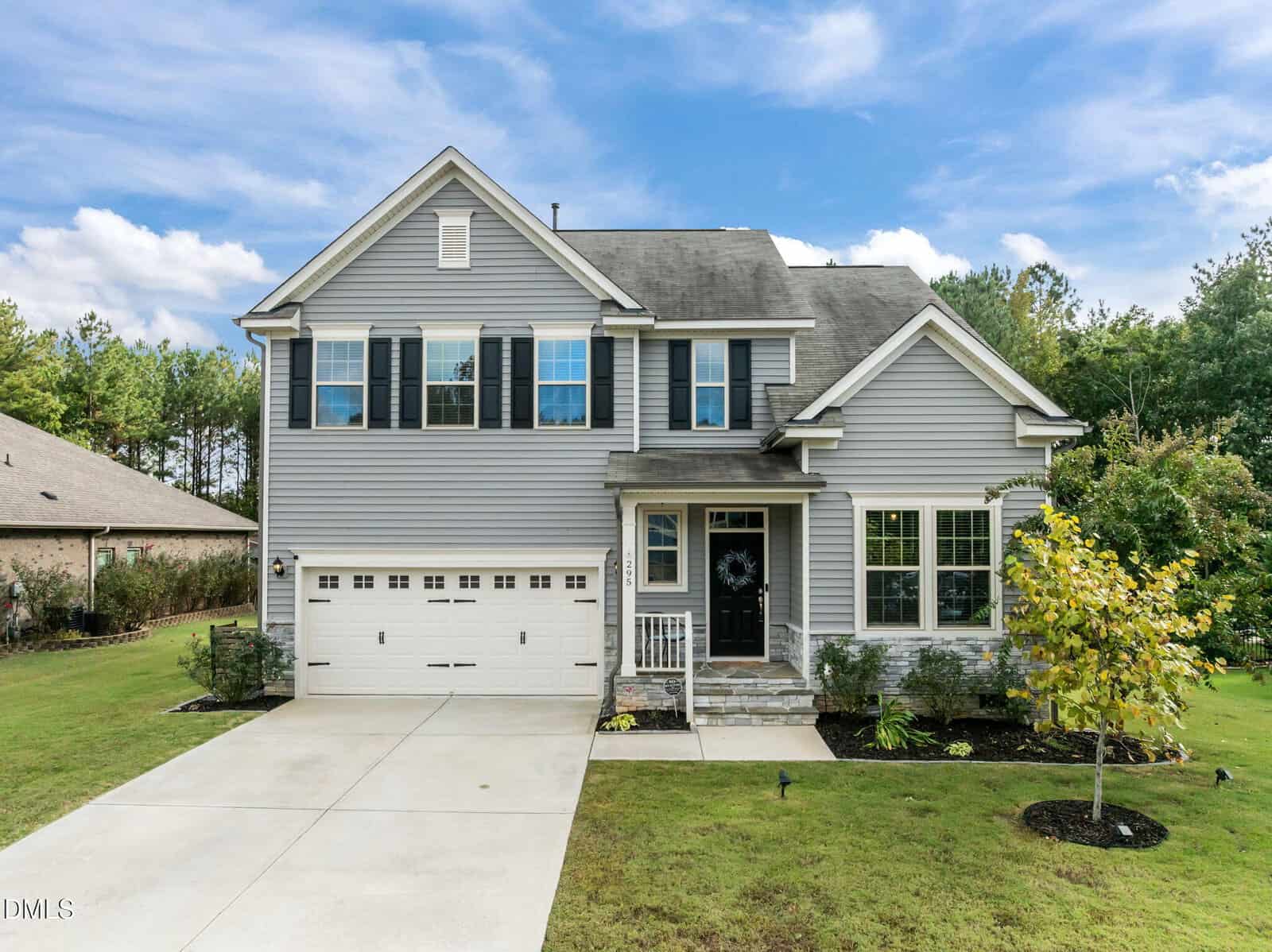 Two-story suburban house with gray siding, black shutters, and a double garage on the left. A small porch with white railings leads to the front door. Neatly landscaped lawn and trees surround the property at 295 Long View Drive in Franklinton.
