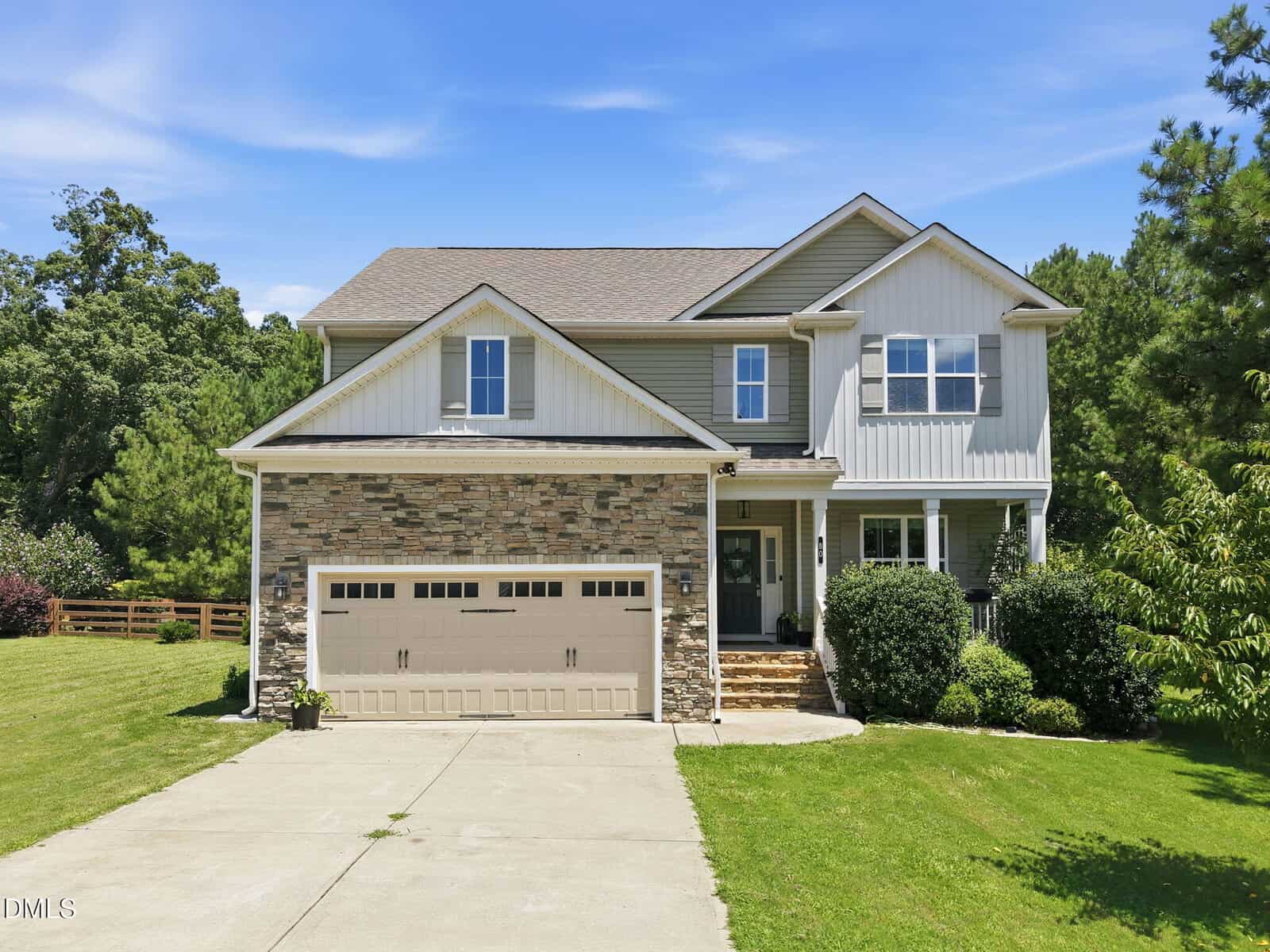 A two-story suburban house at 80 Lockamy Lane in Youngsville features a stone and siding exterior, an attached two-car garage, a concrete driveway, front steps, and a well-kept lawn with bushes and trees surrounding the property under a blue sky.