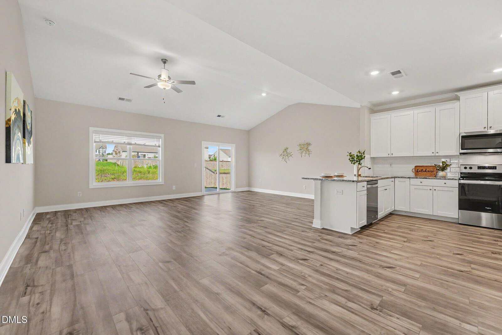 Spacious open-concept kitchen and living area with wood flooring, white cabinets, stainless steel appliances, and large windows letting in natural light.