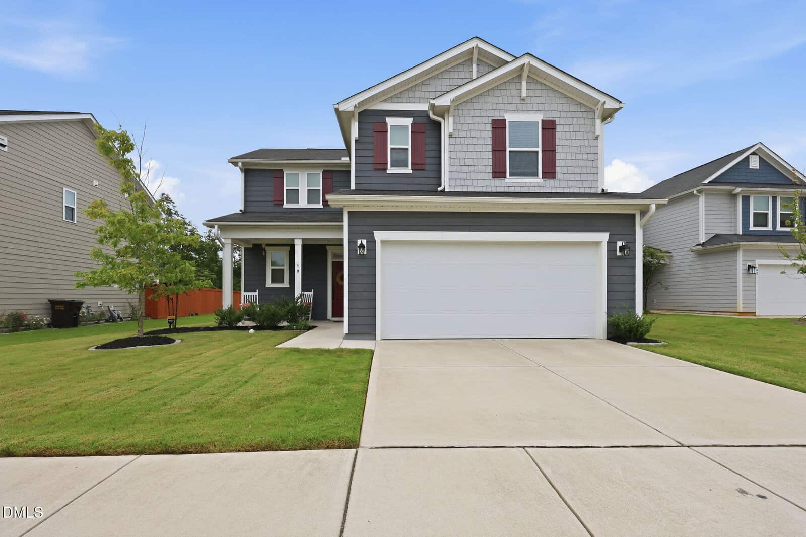 Two-story gray house with white trim and red shutters, attached two-car garage, wide driveway, green lawn, and minimal landscaping under a clear blue sky. Nestled on 50 Purple Aster Street in Youngsville, neighboring houses are visible on both sides.