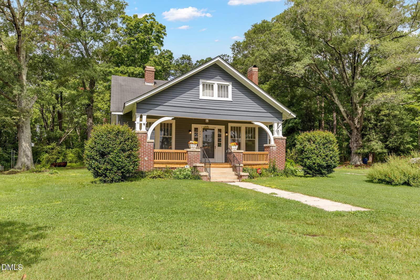 A gray, single-story house with white trim and a front porch sits on a large grassy yard at 280 Edwards Road in Henderson. Brick columns support the porch, and two large bushes flank the entrance. Tall trees are visible in the background.