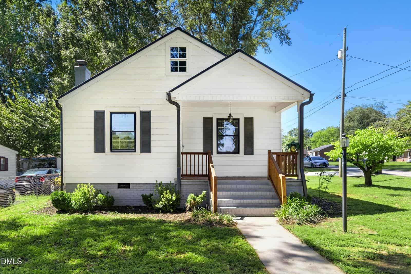 A small white house with dark shutters sits on 119 Rayland Street, Oxford, featuring a front porch with wooden railings, gray steps, and a manicured lawn. Trees and a few houses are visible in the background on a sunny day.