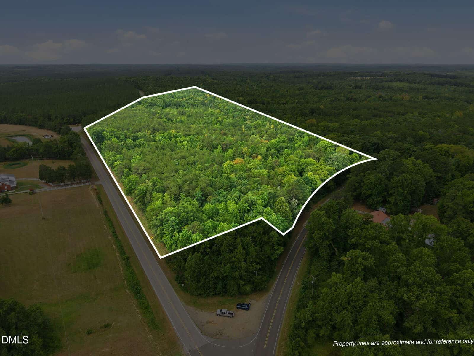 Aerial view of a wooded land parcel outlined in white, located at the intersection of two roads, surrounded by dense forest and fields.