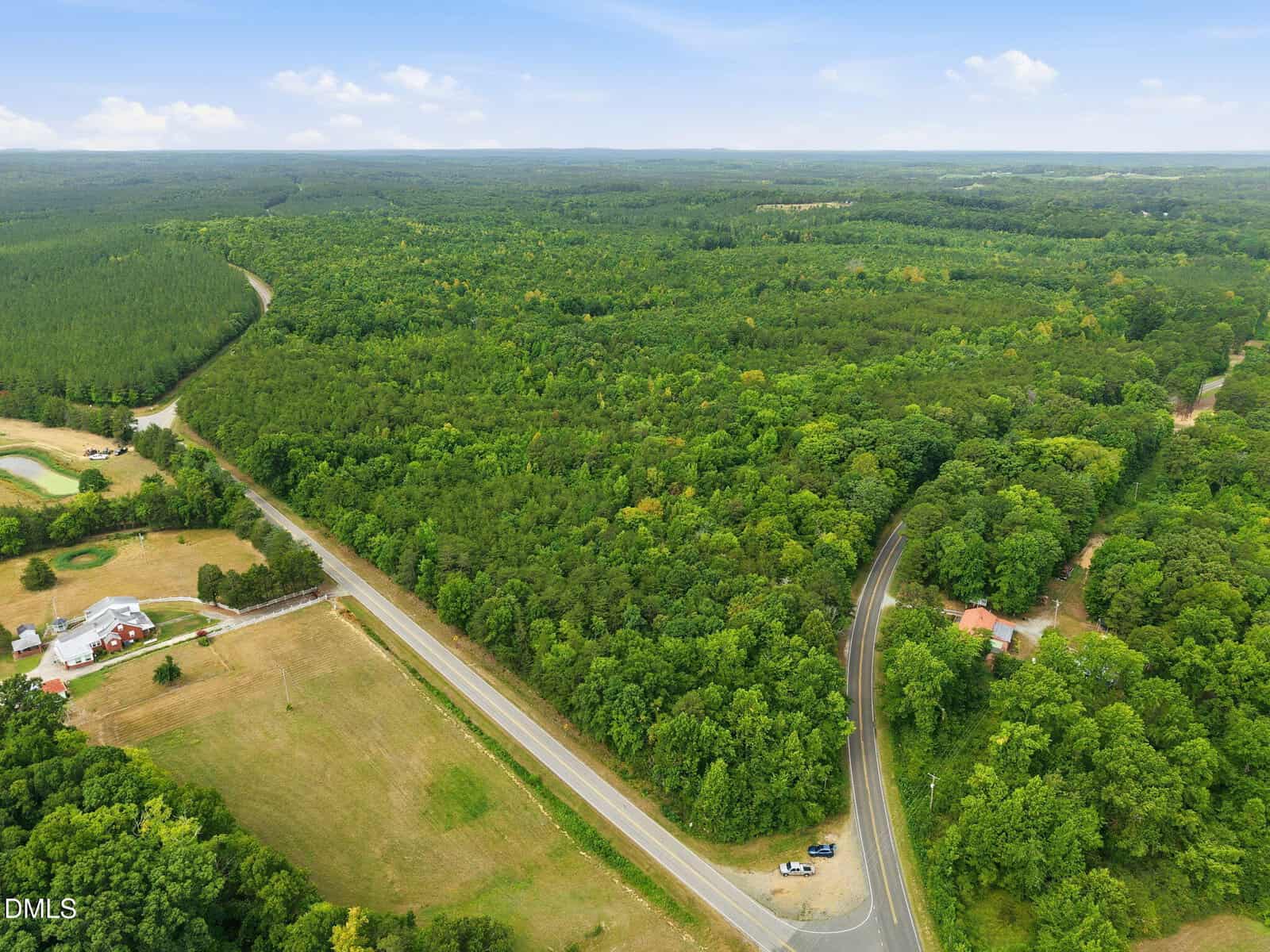 Aerial view of a rural landscape near Oxford, with dense forest, intersecting paved roads including Hwy 49 Road N, a small white house with a red roof, open fields, and several parked vehicles. The sky is partly cloudy.