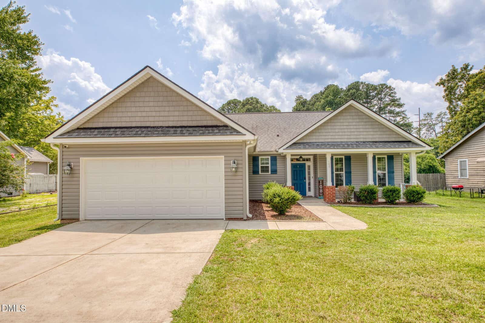 Charming single-story house at 108 Bullock Street in Franklinton, featuring gray siding, white trim, and a two-car garage. A blue front door welcomes you to a small front porch with a brick column, surrounded by a green lawn and a paved driveway under a partly cloudy sky.