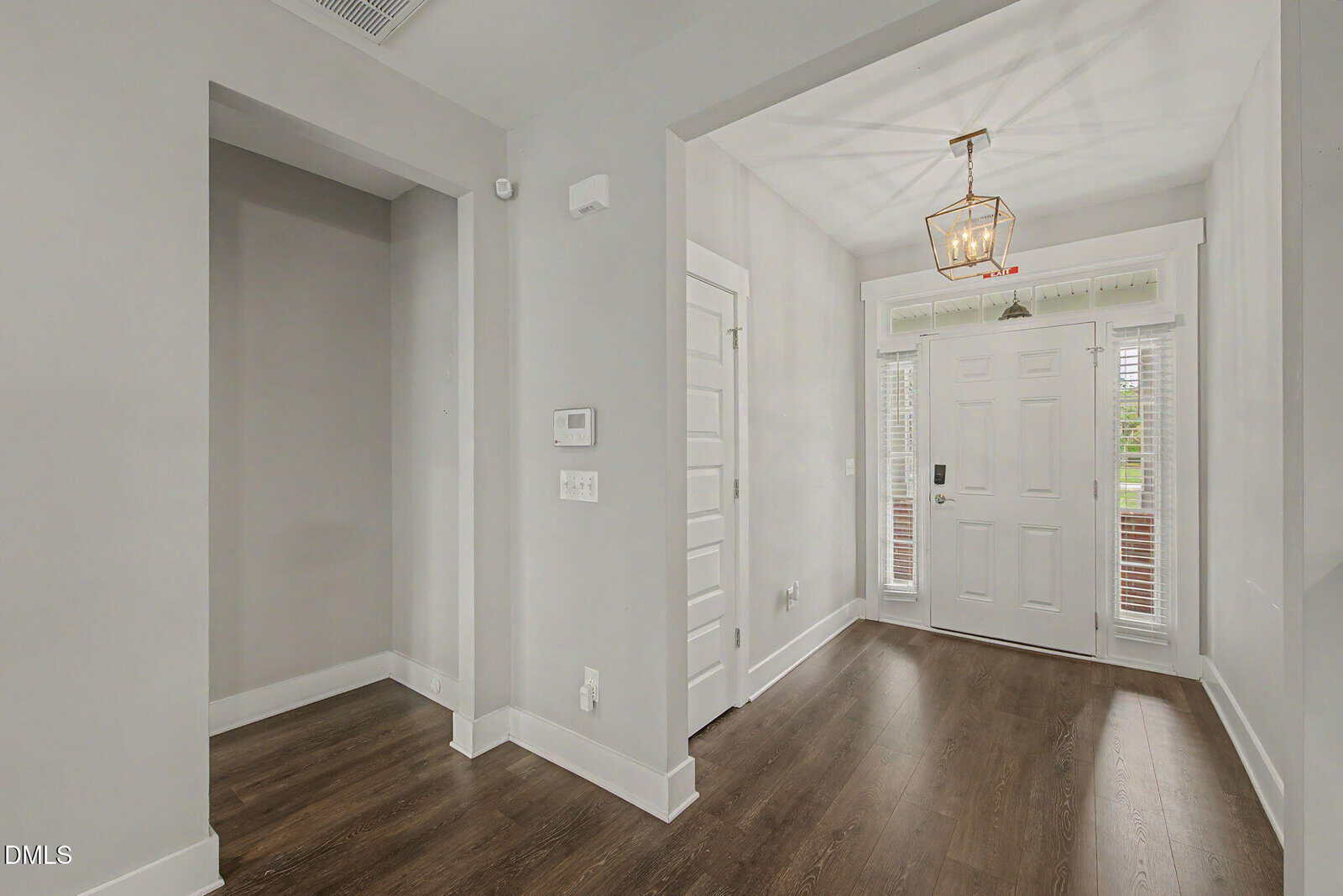 A modern entryway with light gray walls, white trim, dark wood flooring, a white front door with glass panels, and a geometric light fixture hanging from the ceiling.