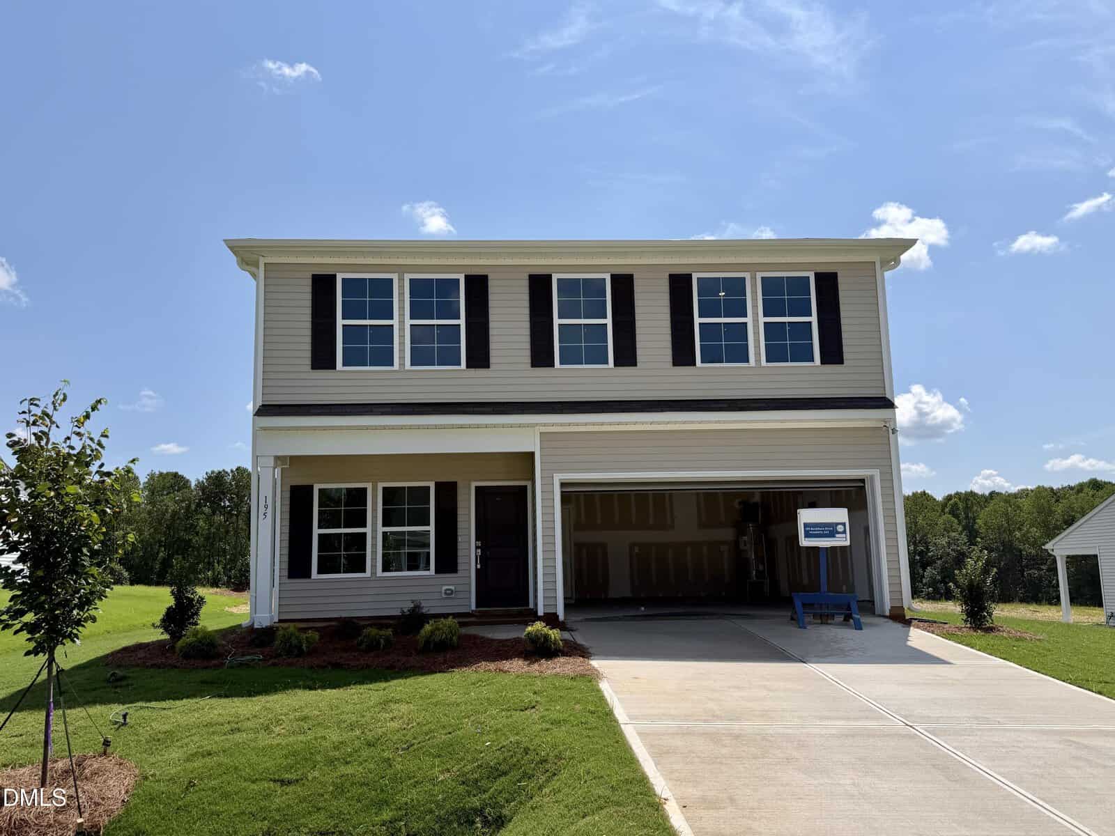 Nestled in the heart of Youngsville, this charming two-story suburban house at 195 Buckthorn Drive features beige siding, dark shutters, and a spacious double garage. The garage door is open, and the freshly landscaped lawn adds to its inviting curb appeal. The sky above is clear and sunny, creating a warm and welcoming atmosphere.