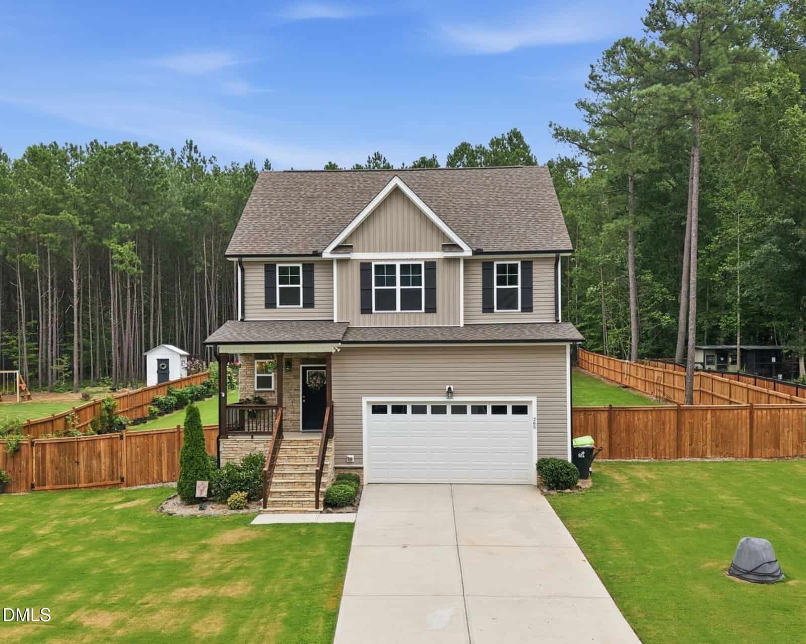 Charming two-story beige house at 265 Sorrel Drive in Franklinton, featuring a covered front porch, attached two-car garage, and fenced backyard. Surrounded by trees and a landscaped lawn, with a concrete driveway leading to the street.