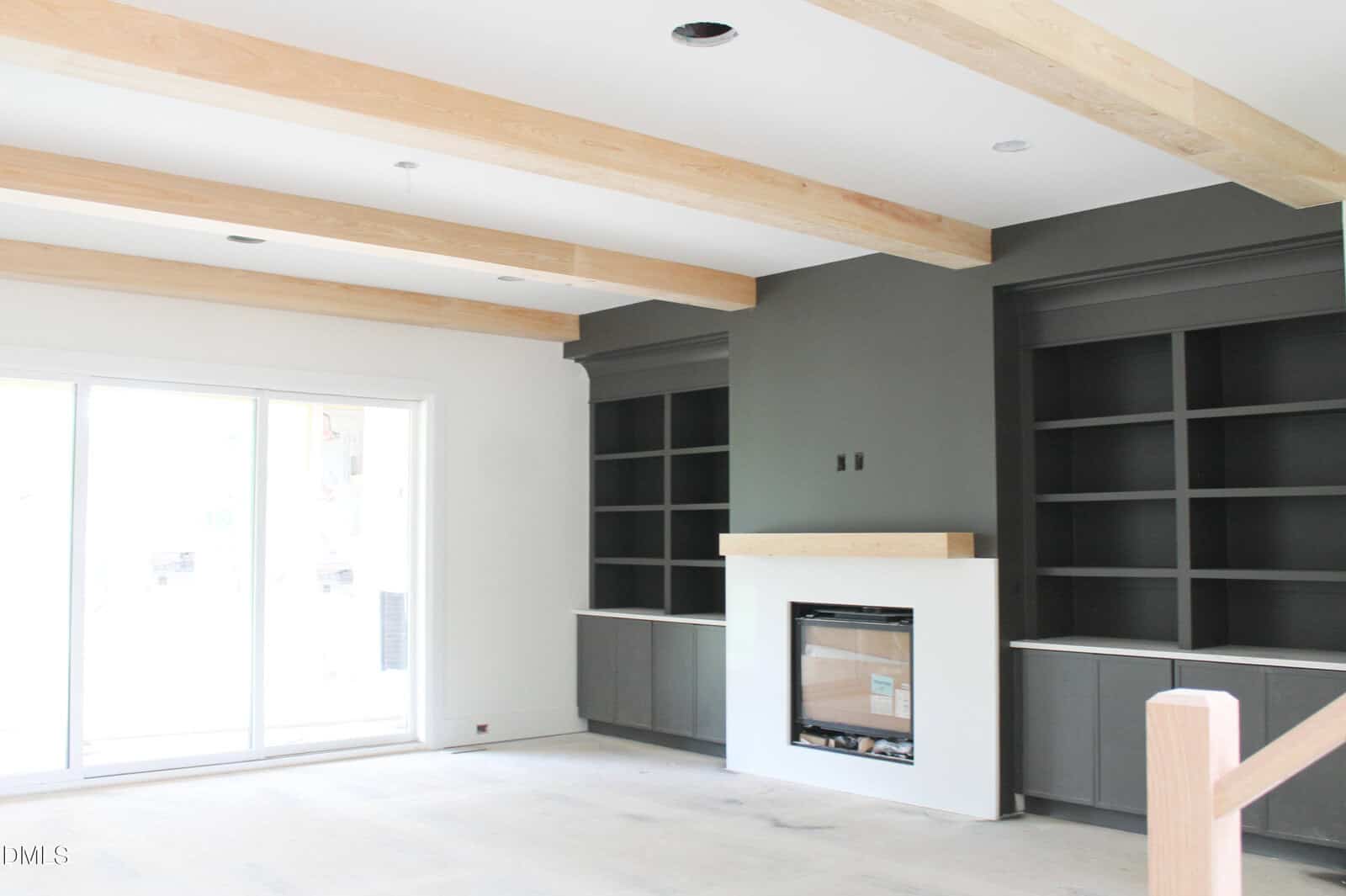 A bright living room with light wood ceiling beams, a gray accent wall with built-in shelves, a fireplace, and large sliding glass doors letting in natural light.