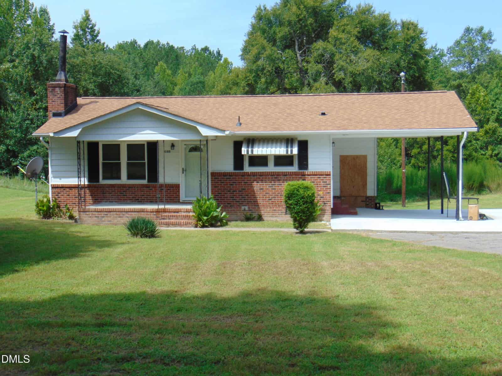 Charming single-story brick house on 3155 Kelly Road, Henderson, featuring a covered front porch, carport, and chimney. The yard boasts green grass and small shrubs, with trees and woods providing a scenic backdrop.
