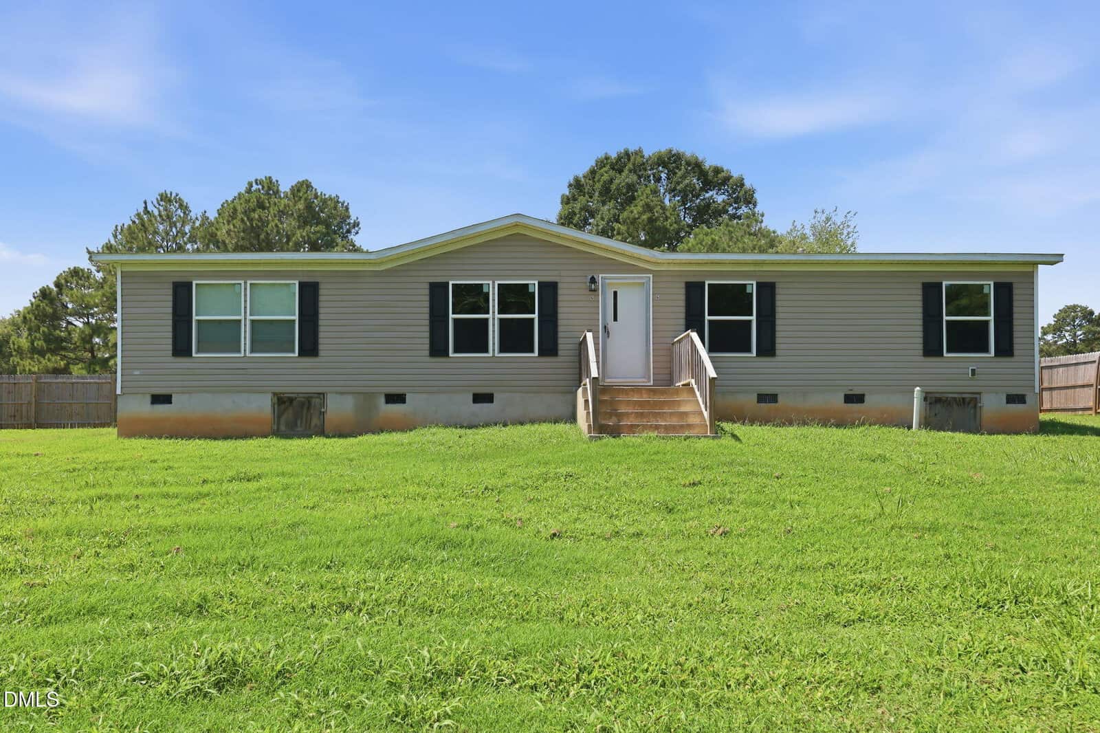 A beige, single-story manufactured home with black shutters and a small front porch sits on a grassy lawn at 6 A F Moore Road in Spring Hope, with trees and a wooden fence in the background under a blue sky.