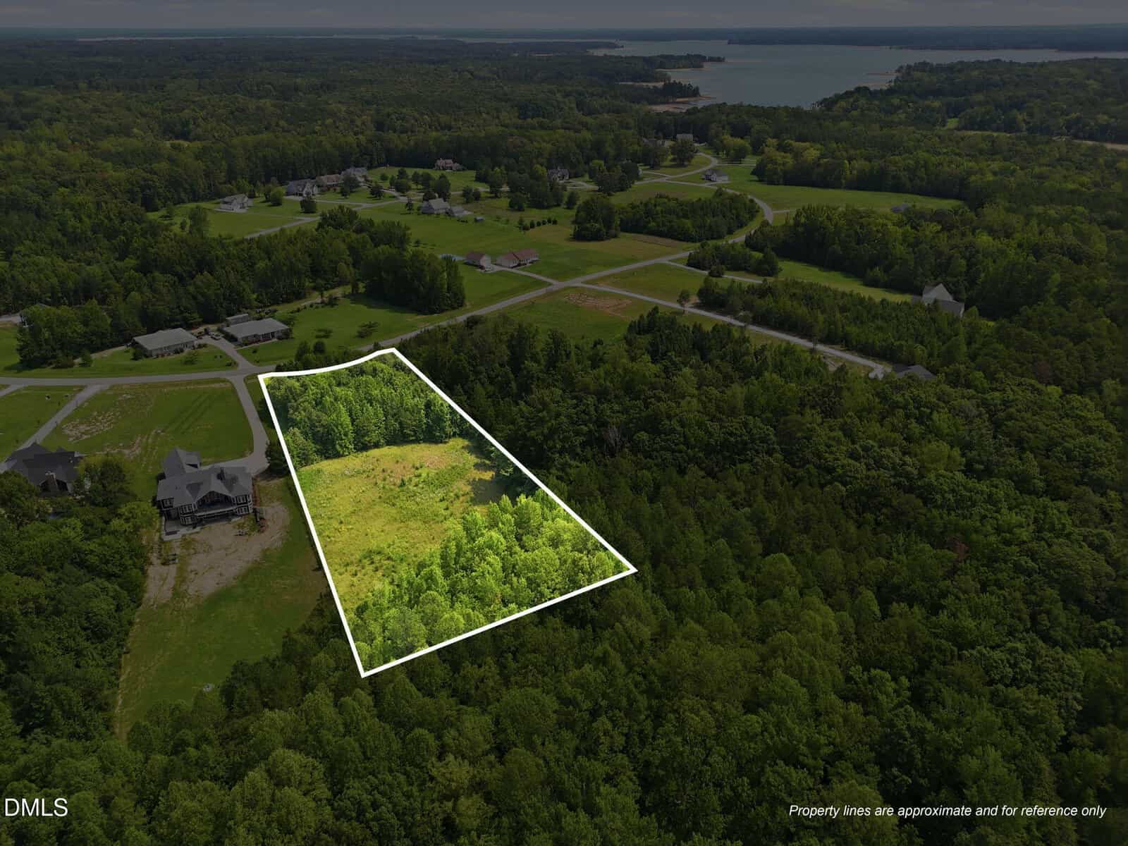 Aerial view of a wooded lot with a clearing, outlined in white, in a rural residential area with scattered houses, roads, and distant water. The property lines are marked for reference only.