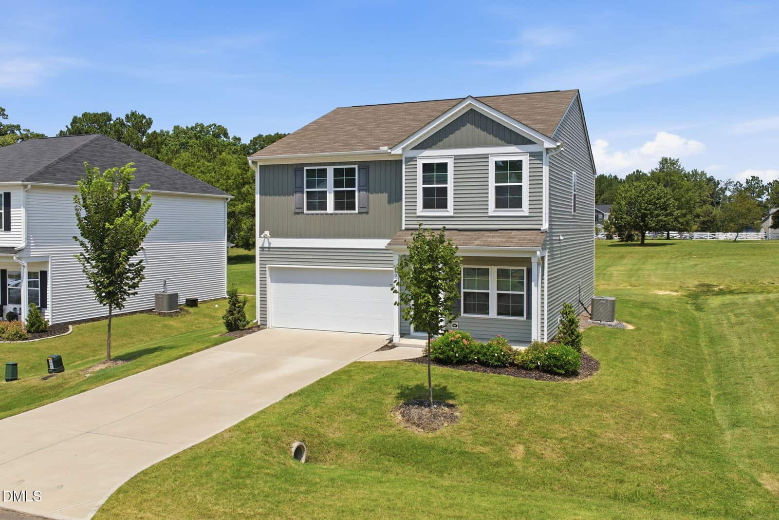 Two-story suburban house with gray siding, white trim, and attached two-car garage located on 40 Spotted Bee Way in Youngsville. Concrete driveway, small front yard with two young trees, and surrounding grassy lawn. Clear blue sky and neighboring houses are visible.