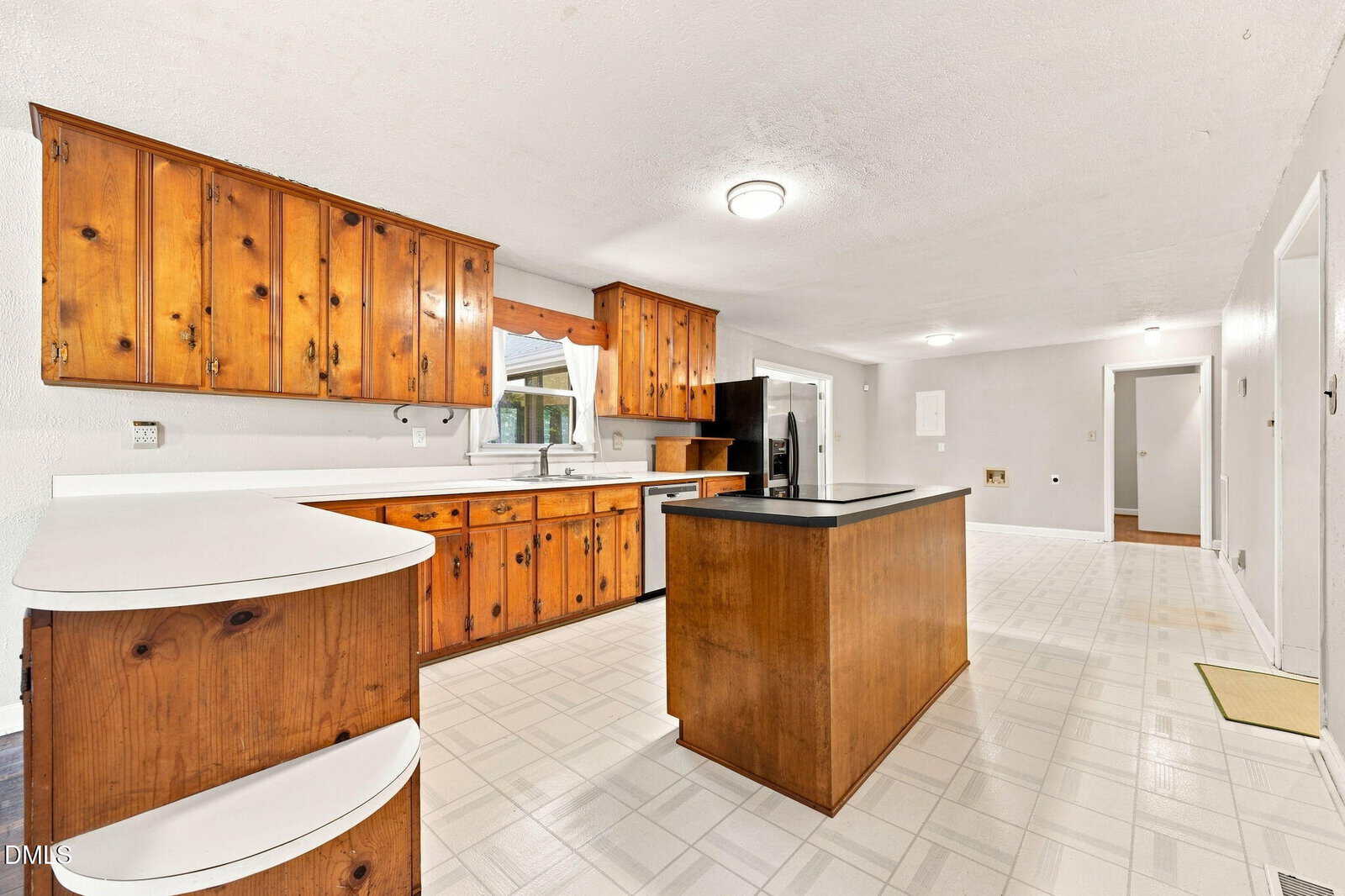 Spacious kitchen with wood cabinets, white countertops, a central island, and white tile flooring. Stainless steel appliances and a window above the sink provide a bright, inviting atmosphere.