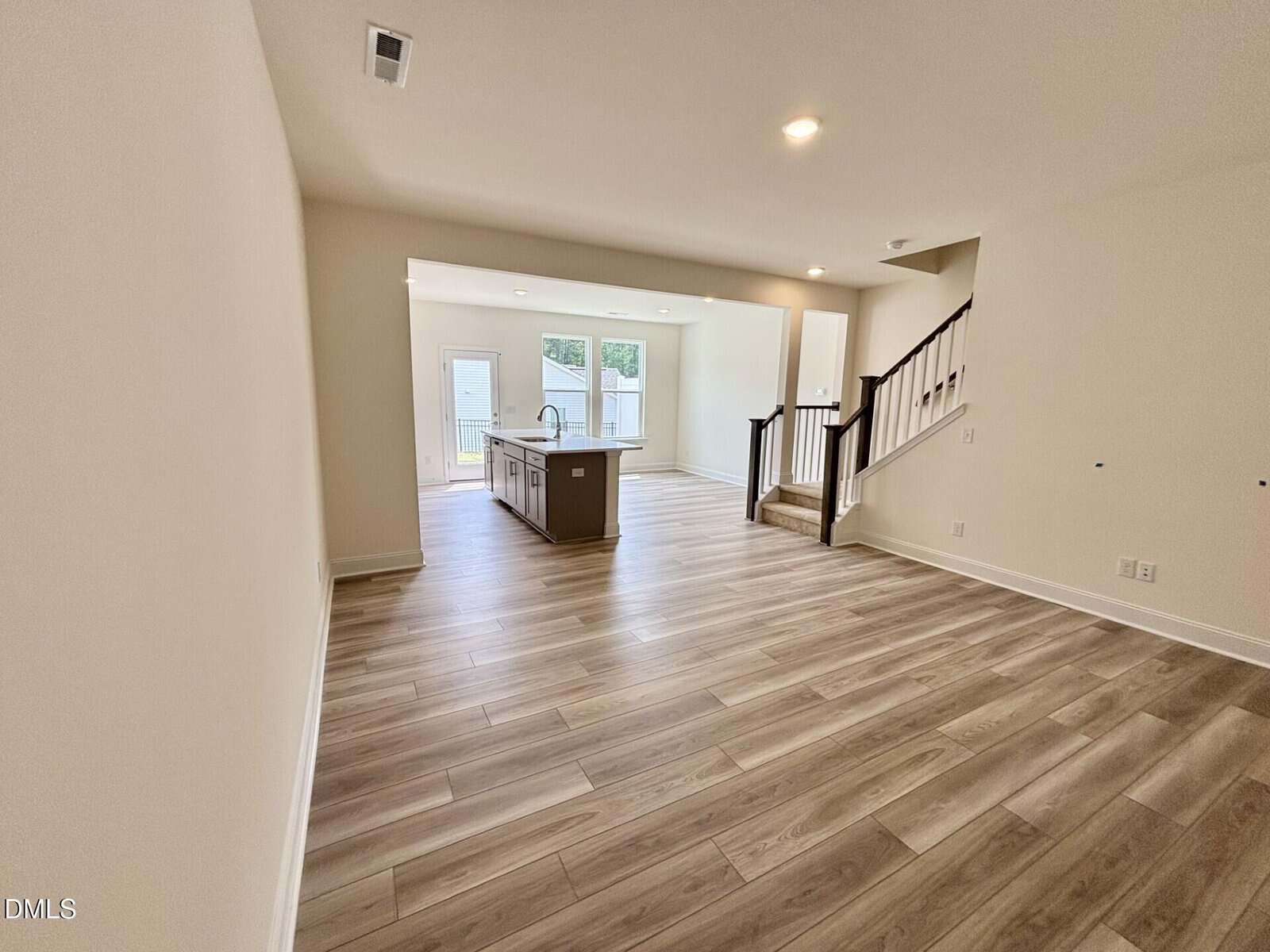Open-concept living area with light wood floors, a modern kitchen island, sliding glass doors to a backyard, and a staircase with dark railings leading upstairs.