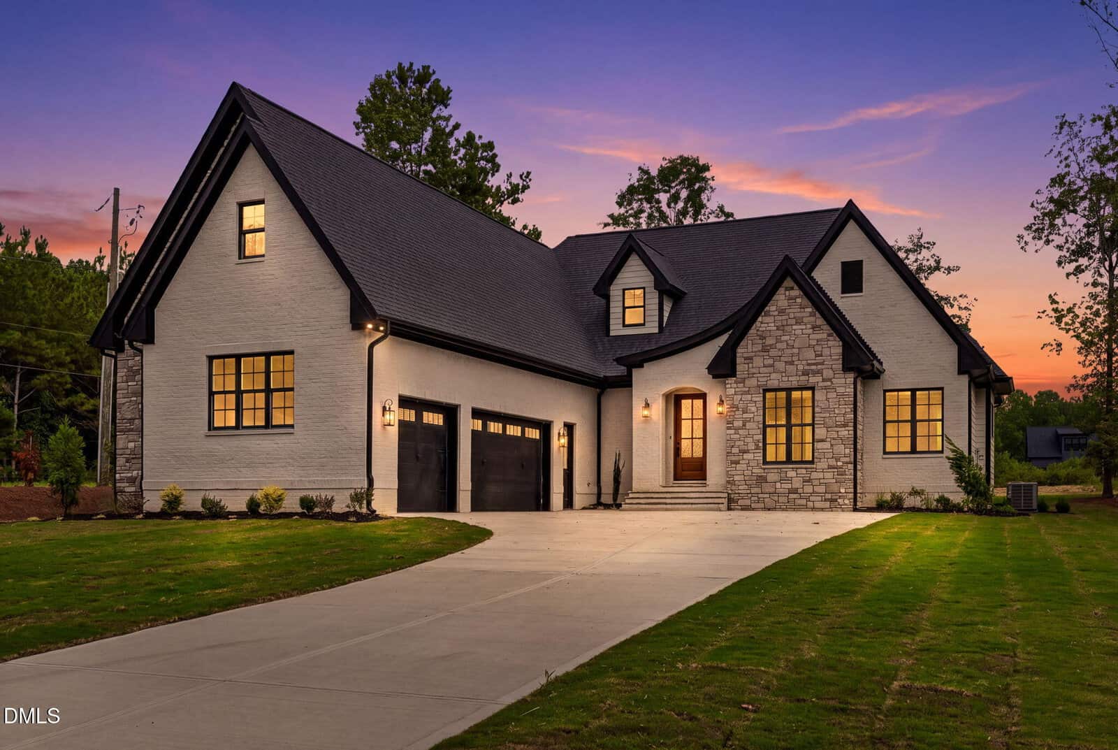 Modern two-story house with stone and white brick exterior, black trim, large windows, two-car garage, and a wide driveway at 5 Harvest View Way in Franklinton, set against a sunset sky with green lawn and trees in the background.