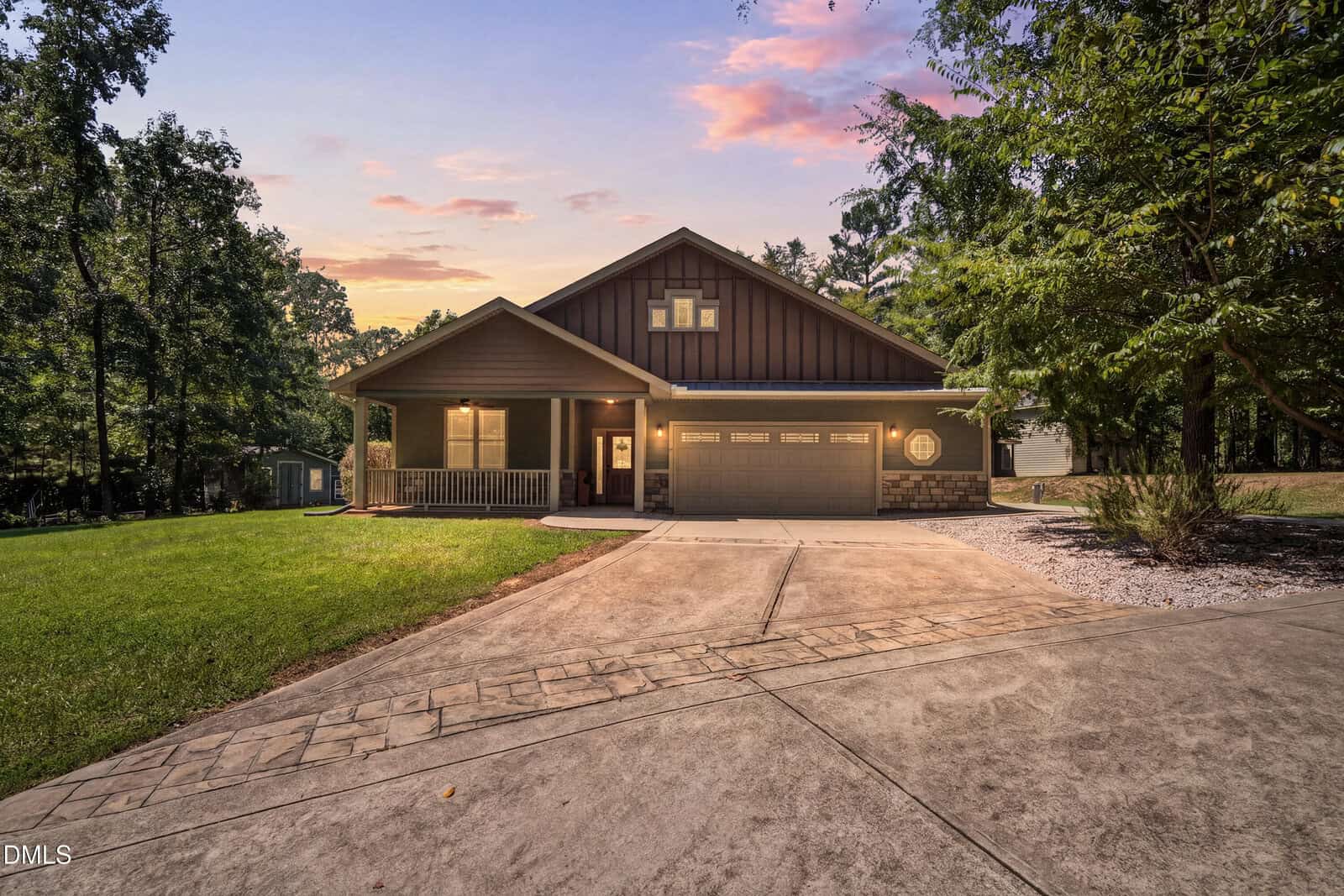 A modern single-story house at 127 Sacred Fire Road, Louisburg, featuring a porch, two-car garage, and a wide driveway, surrounded by trees and grass at sunset.