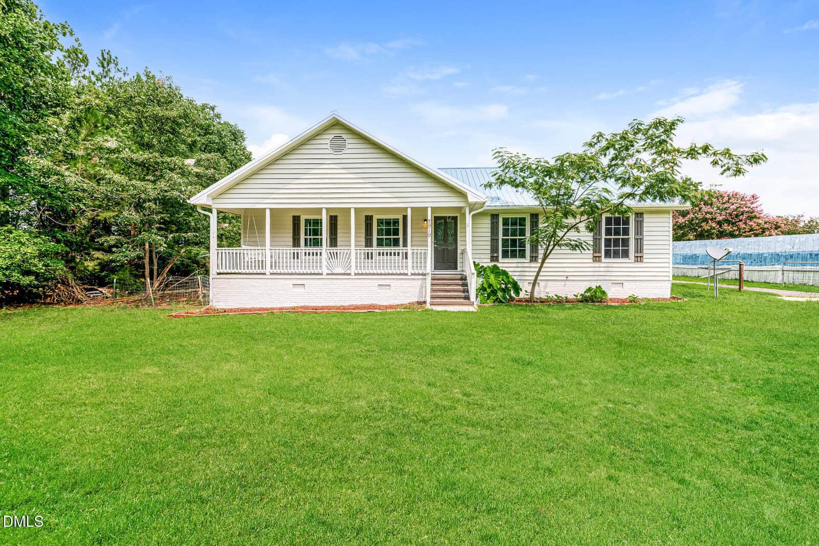 Charming white single-story house at 2919 Glebe Road in Henderson, featuring a welcoming front porch and green lawn, surrounded by trees under a blue sky. A paved driveway runs along the right side of the house.